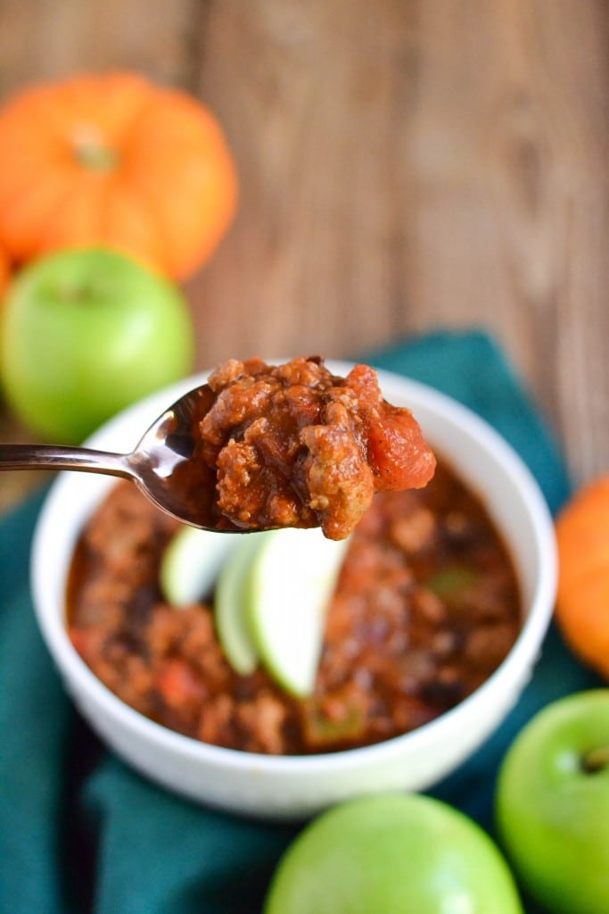 A spool full of turkey pumpkin chili over a bowl of chili and apples. 