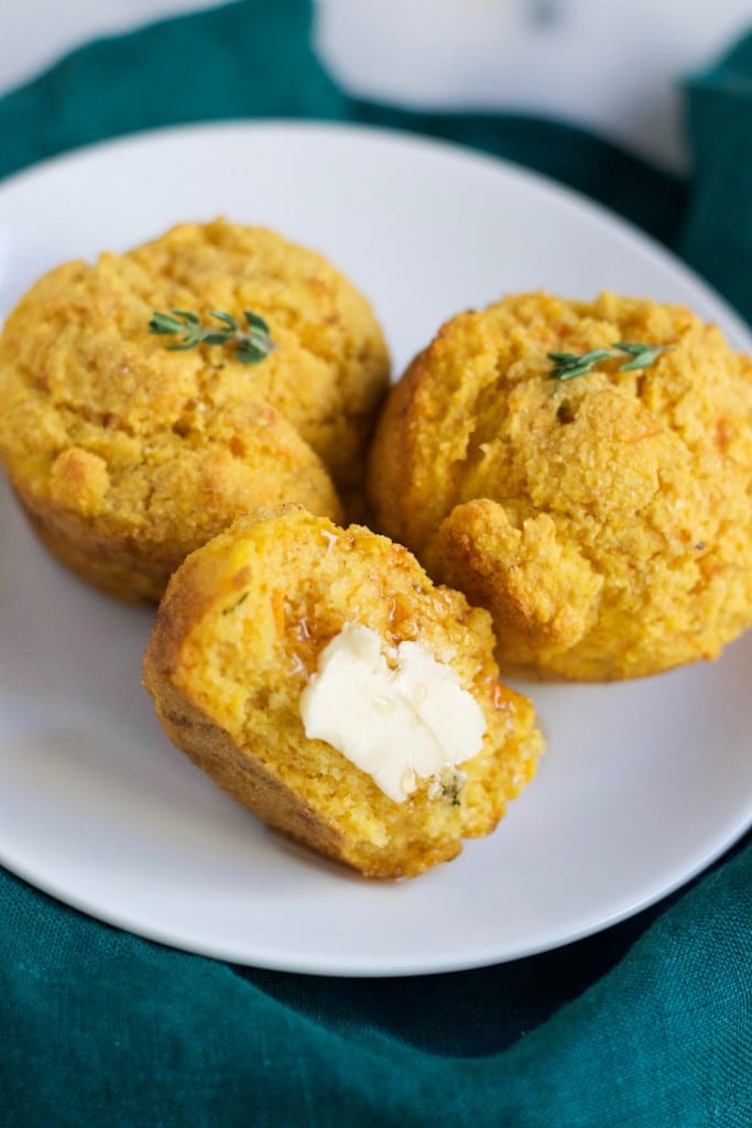 A plate with three sweet potato cornbread muffins with one cut in half with butter on it.