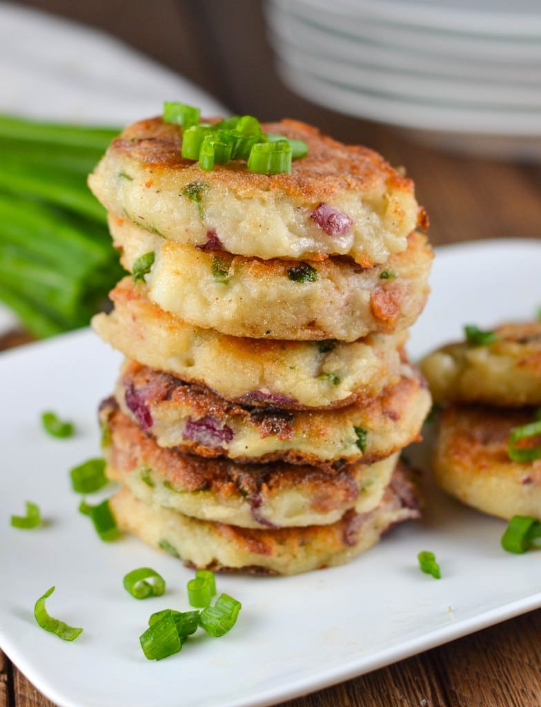 A stack of mashed potato cakes studded with bacon and topped with chopped green onion. 