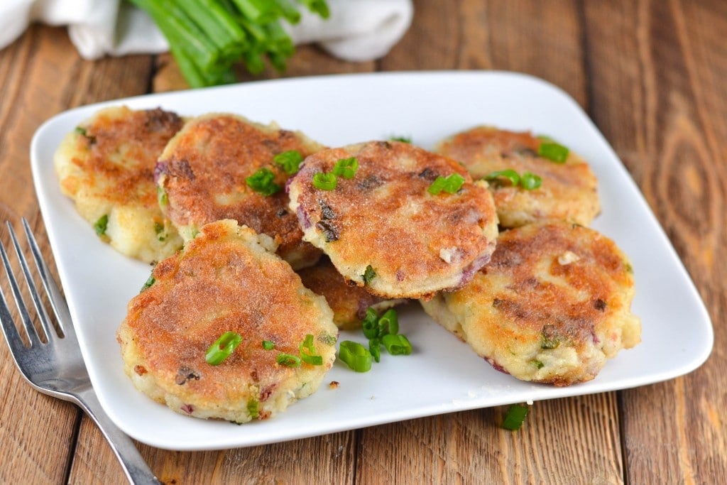 A pile of mashed potato cakes with green onions on a platter with a fork. 