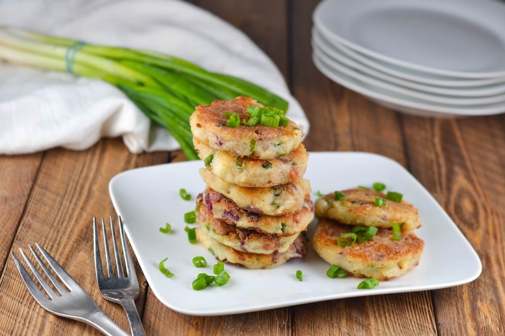 A plate filled with a stack of mashed potato cakes topped with chopped green onions. 