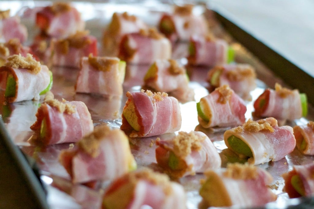 Bacon wrapped apples with a sprinkle of brown sugar on top spaced out on a sheet pan lined with aluminum foil. 