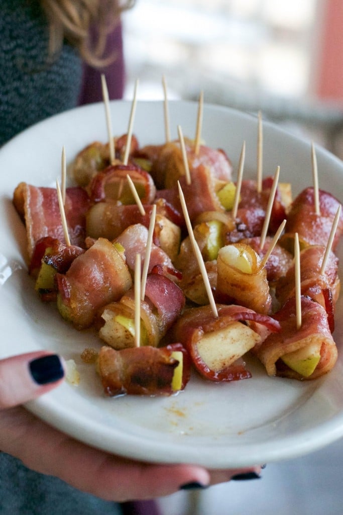 A woman holding a platter of brown sugar bacon wrapped apple bites with cocktail picks sticking out of them.