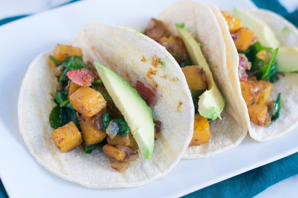 A plate with three butternut squash, bacon, spinach and avocado tacos on it. 