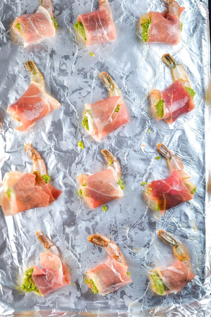 Prosciutto wrapped shrimp spaced out on a sheet pan lined with aluminum foil. 