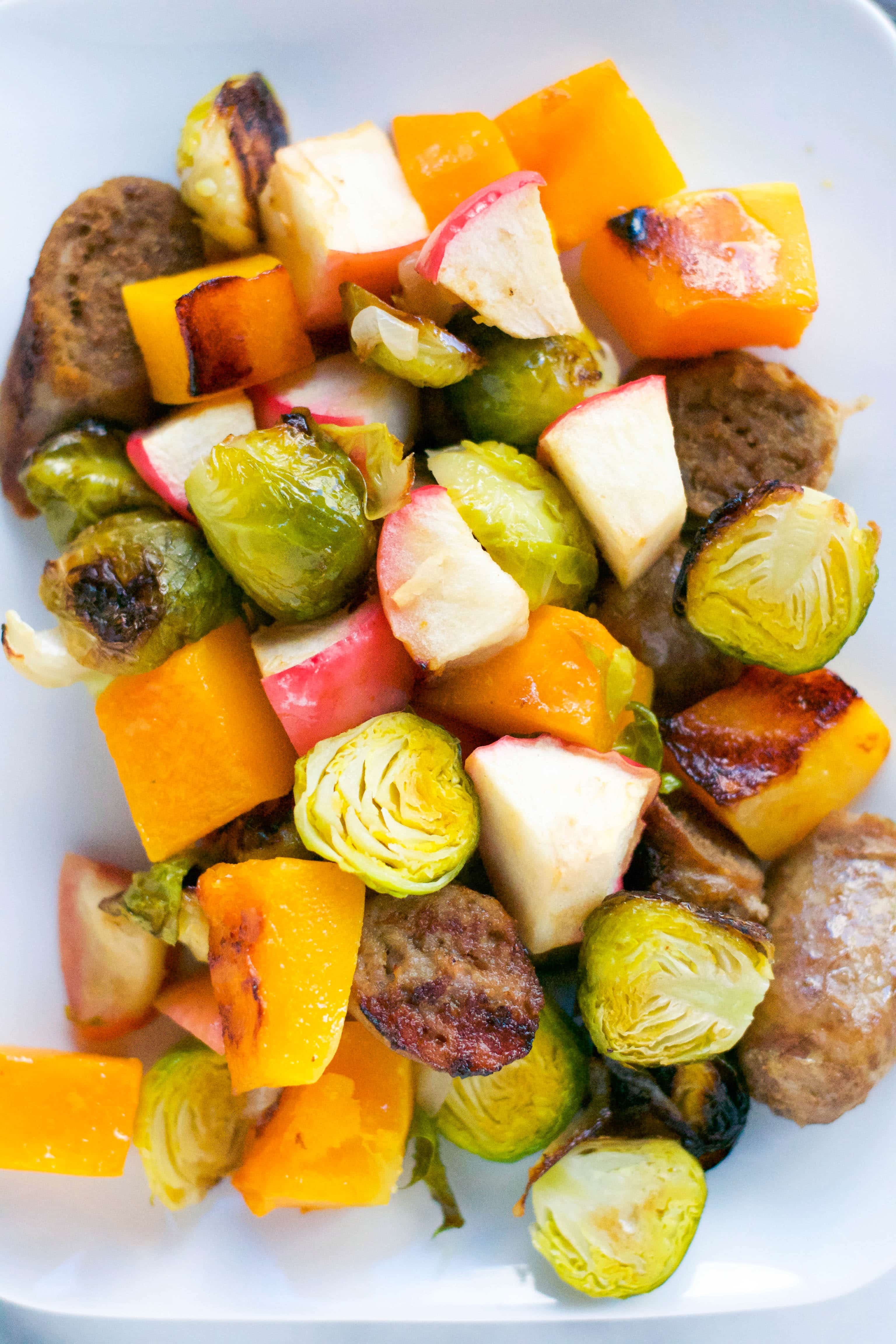 An overhead view of roasted brussels sprouts, apples, chicken sausage slices, and butternut squash pieces. 