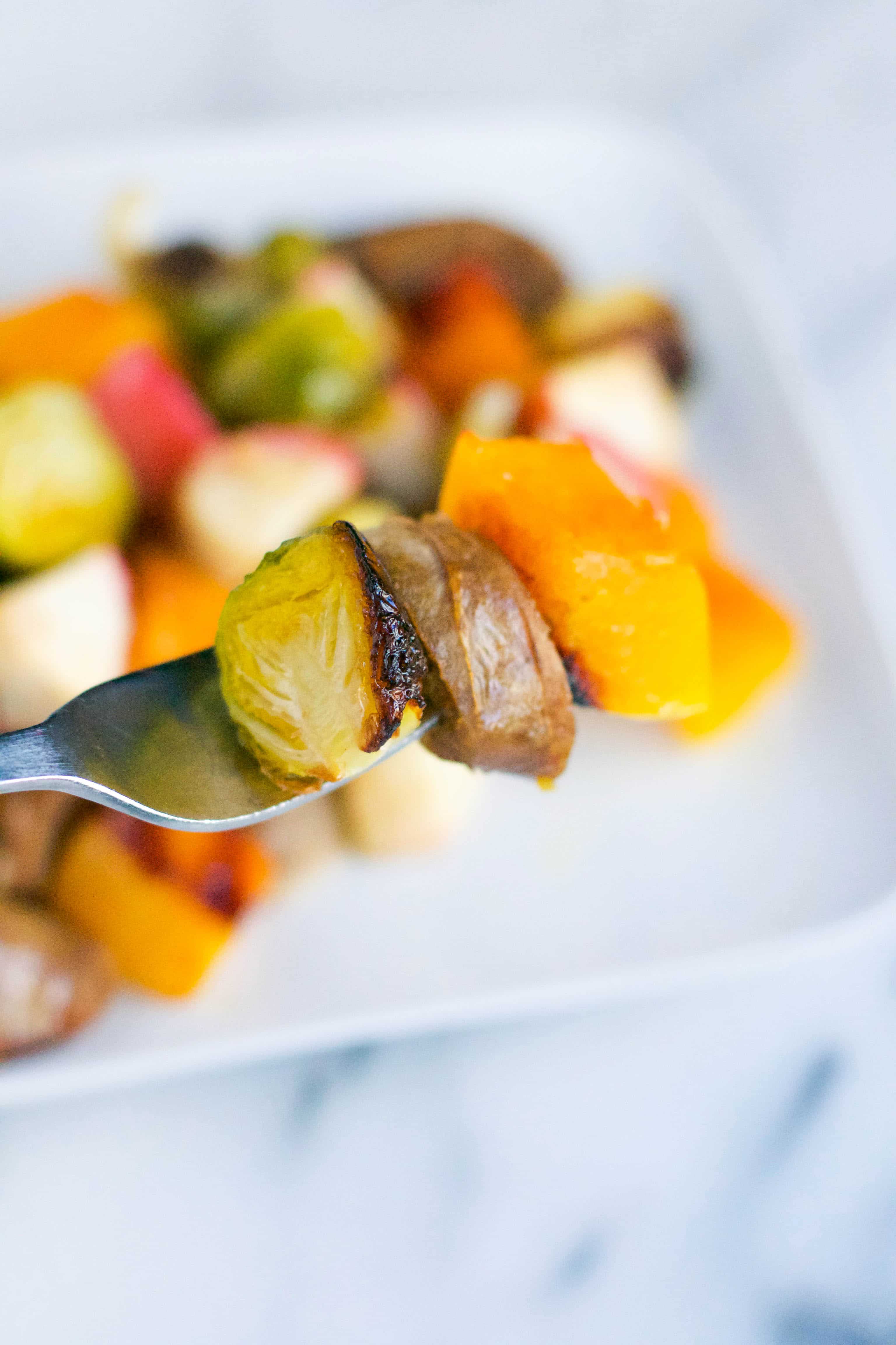 A fork with roasted brussels sprout, a piece of chicken sausage, and a piece of roasted butternut squash. 