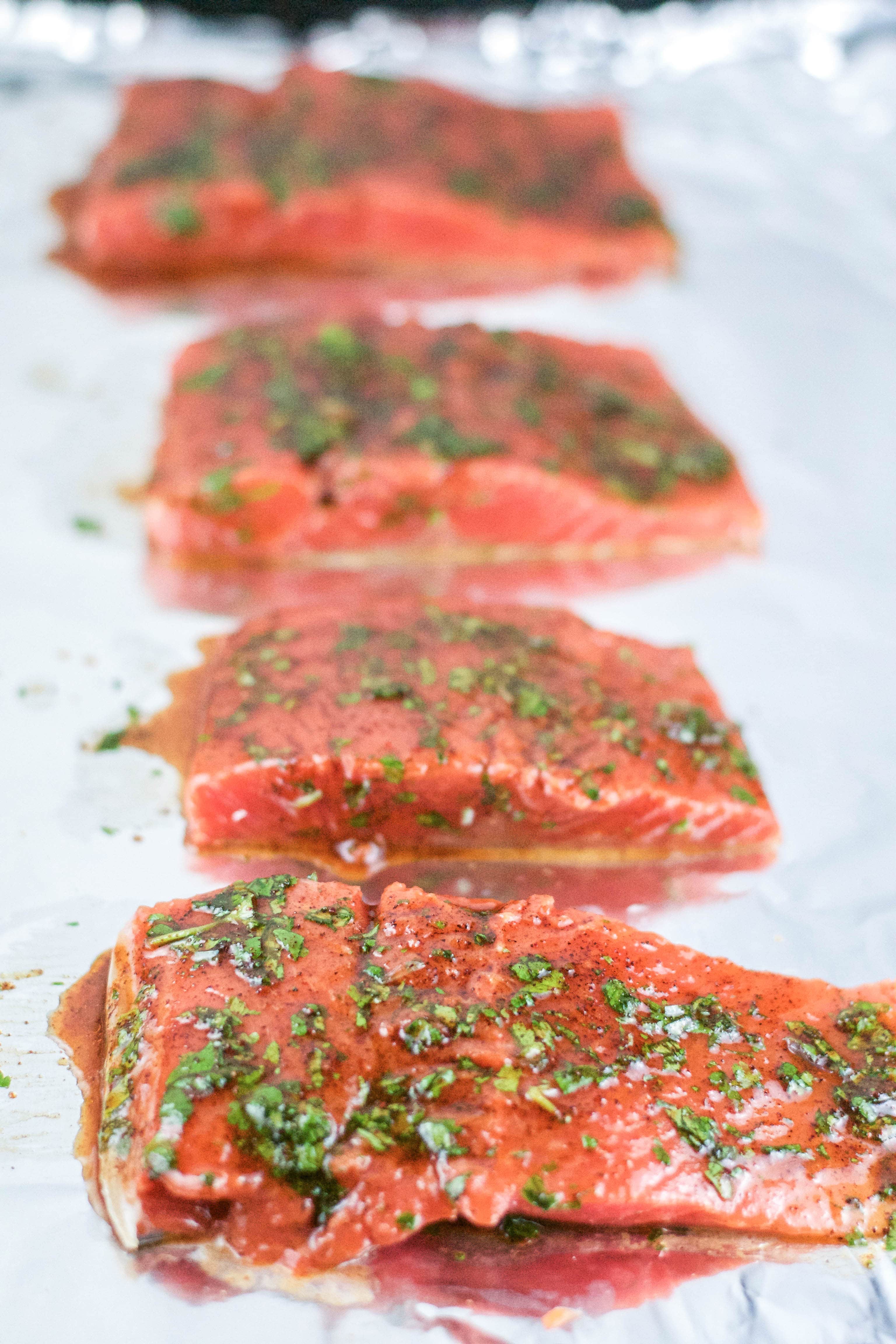 Raw salmon portions with cilantro and honey glaze on a baking sheet lined with aluminum foil. 