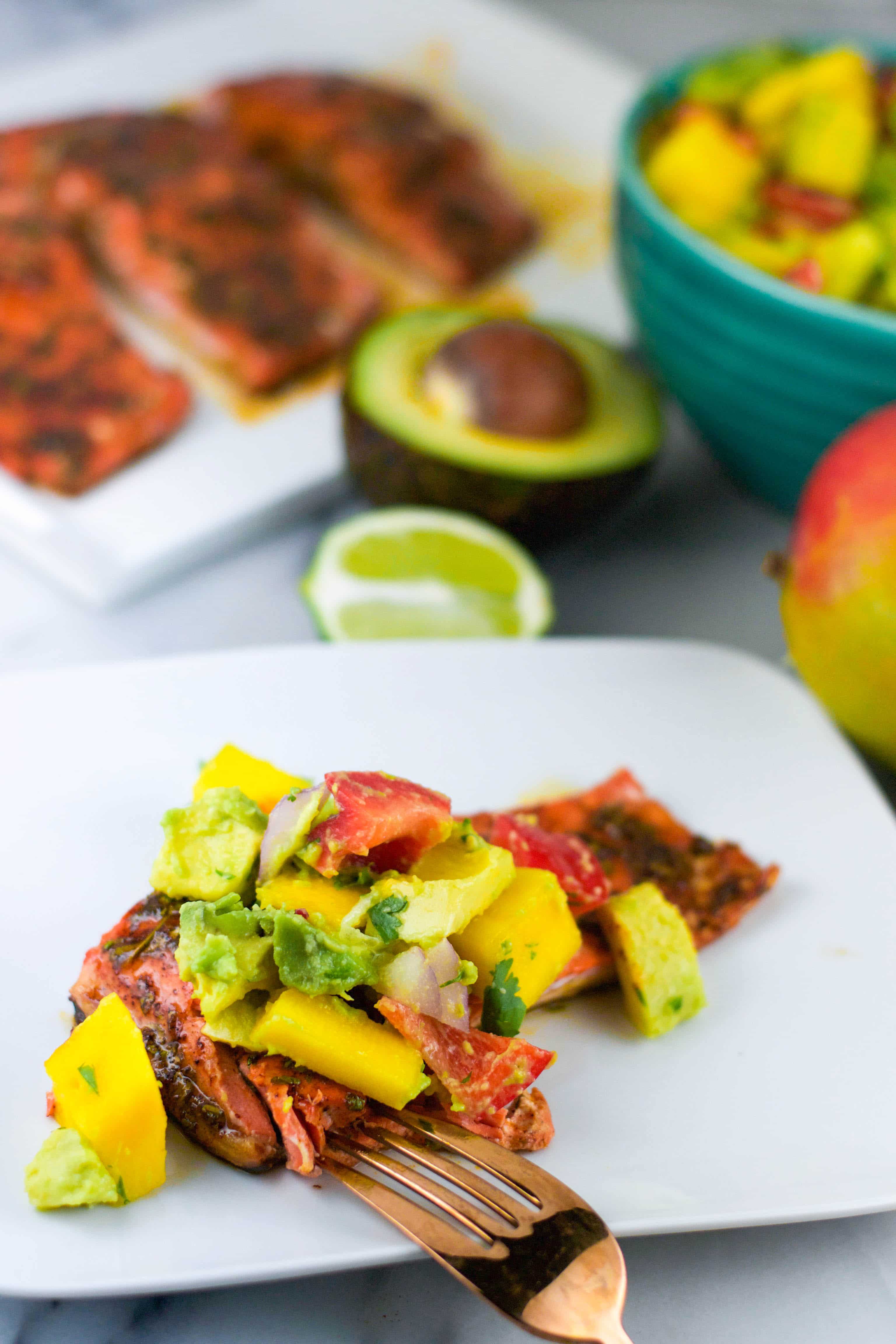 a plate of salmon with avocado mango salsa on top with a fork next to it. 