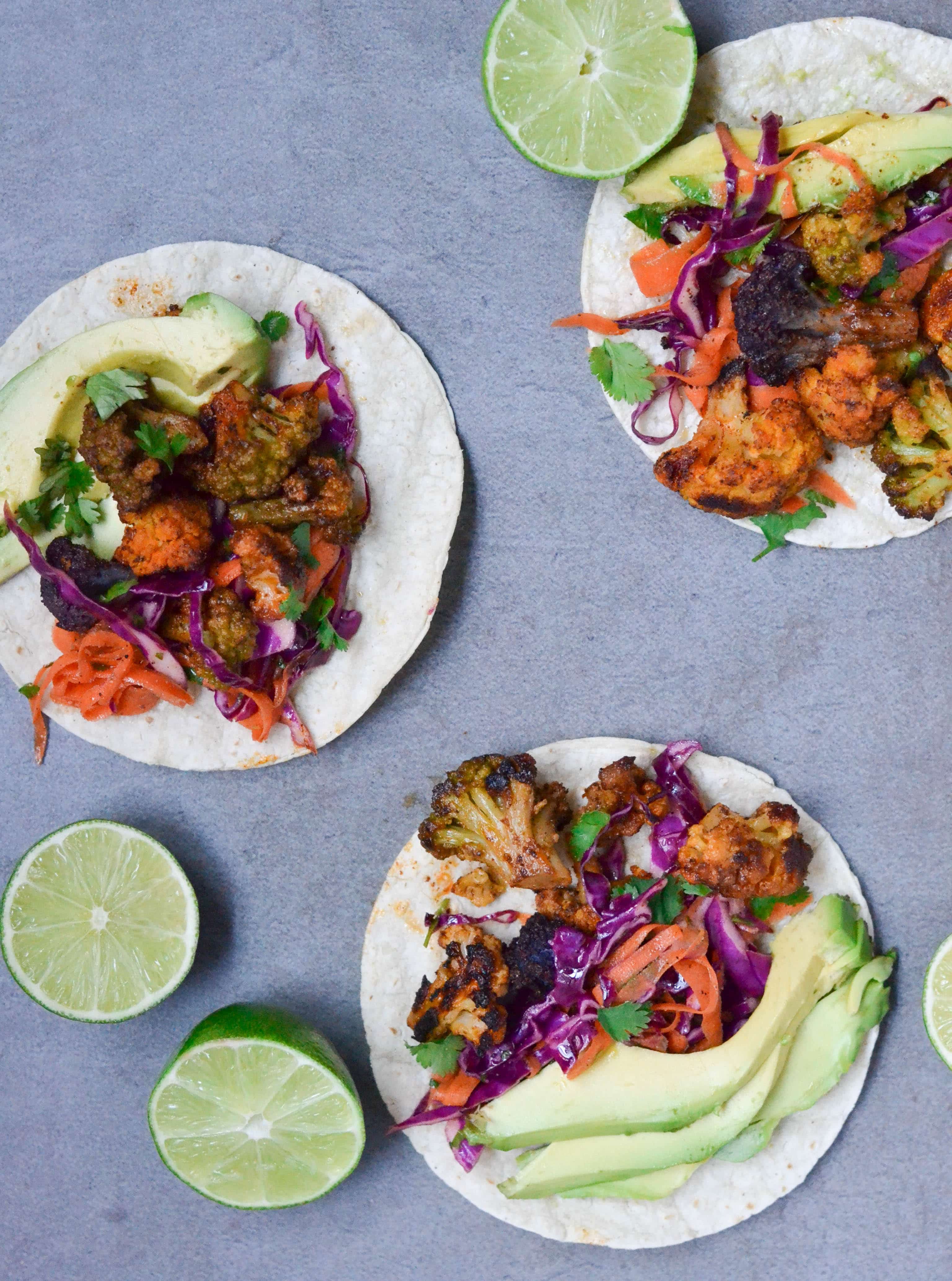 Three Roasted Cauliflower Tacos on a table with lime halves scattered around.