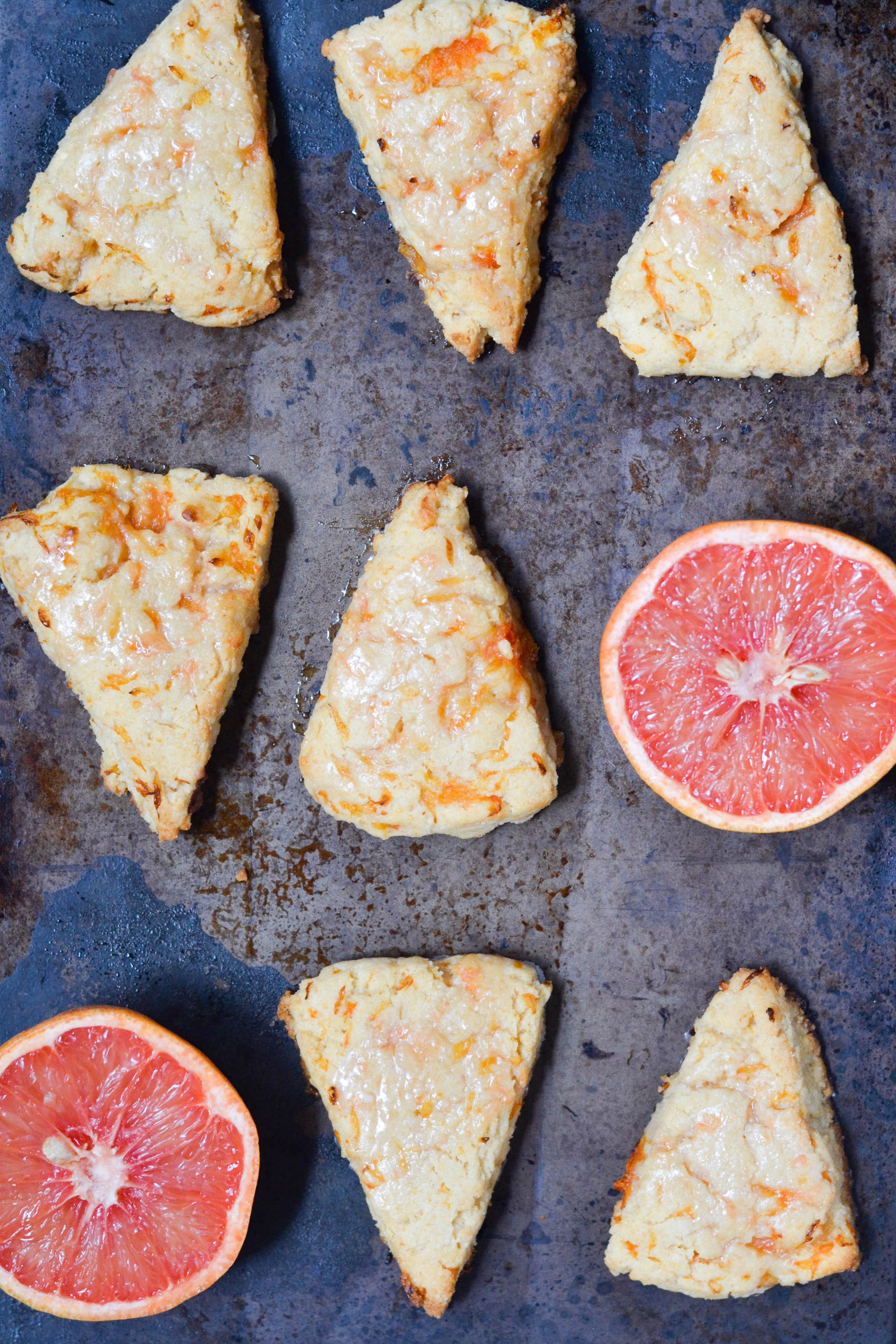 Gluten-free vegan grapefruit scones on a baking sheet with two grapefruit halves. 