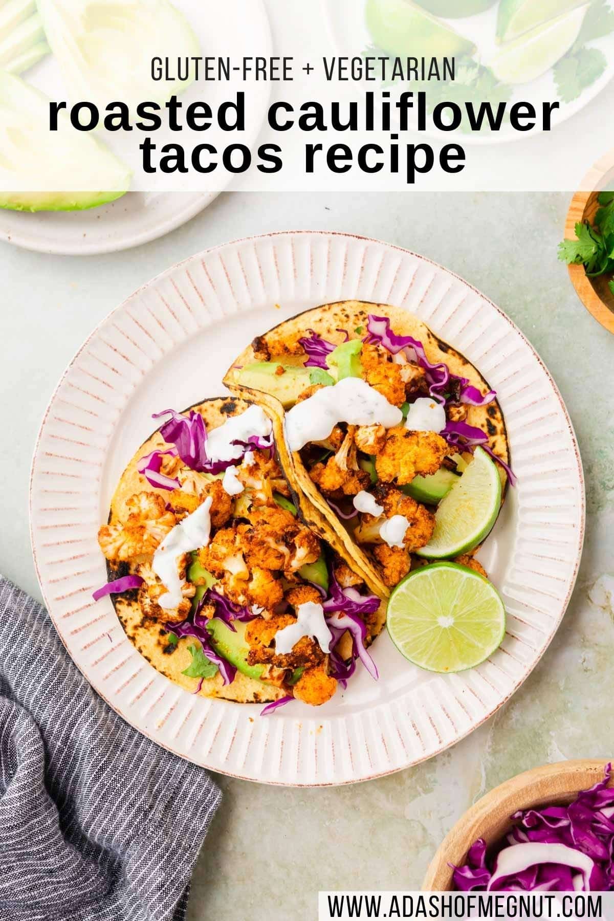 An overheard view of a plate of two cauliflower tacos topped with purple cabbage, lime wedges, avocado slices, and cilantro.