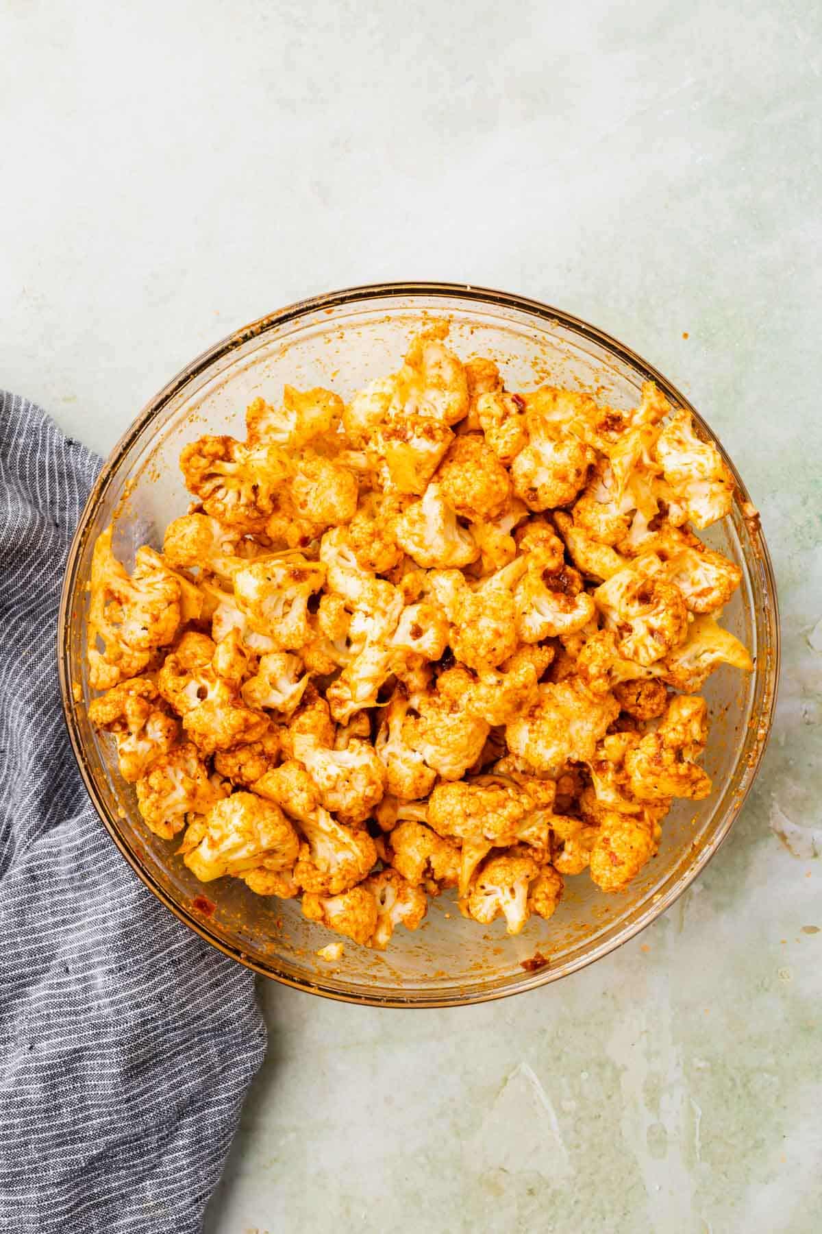 Cauliflower florets in a glass mixing bowl mixed with taco seasoning and adobo sauce.