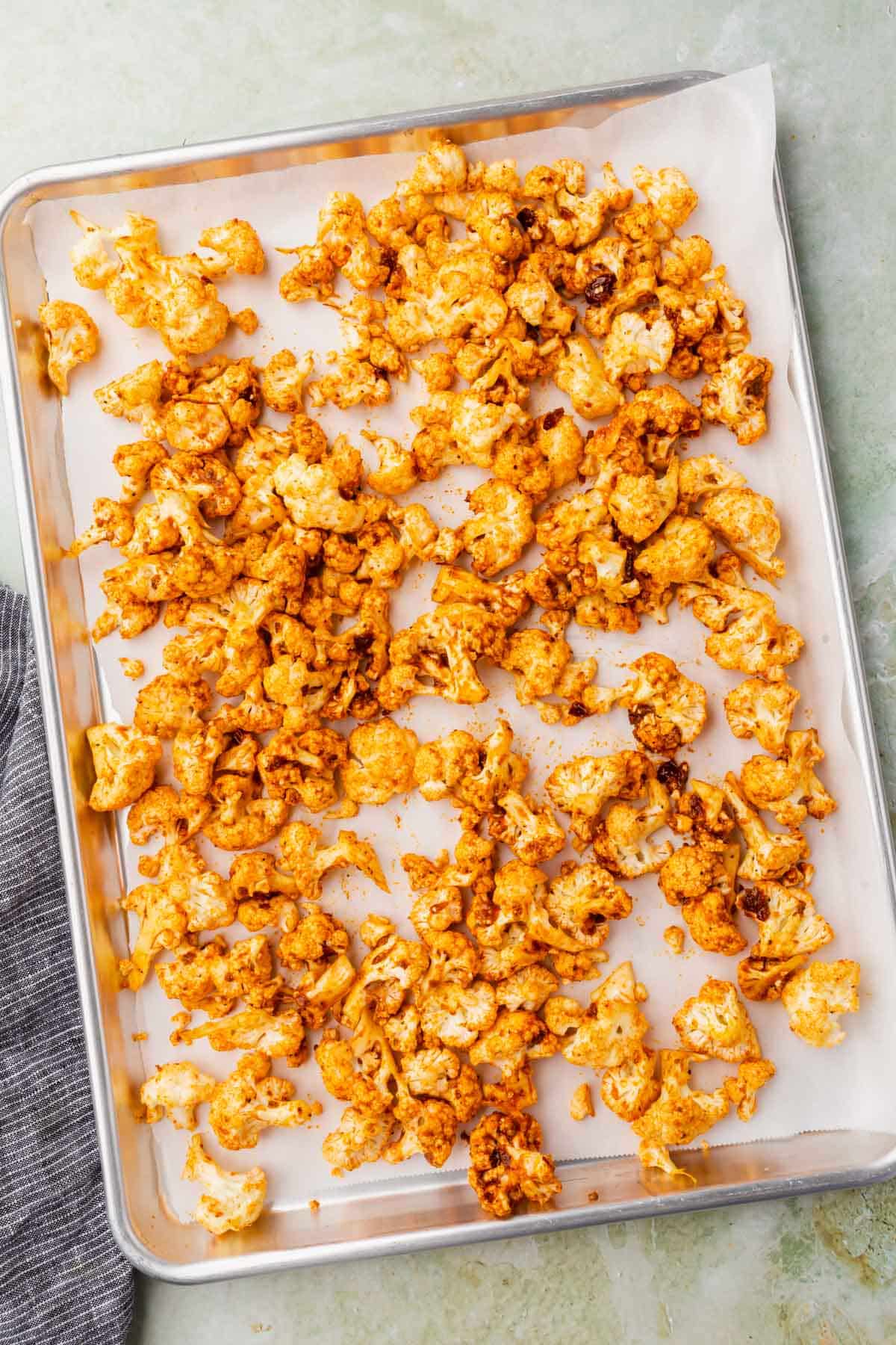 Cauliflower florets on a parchment lined baking sheet that have been tossed in a red sauce mixture before baking.