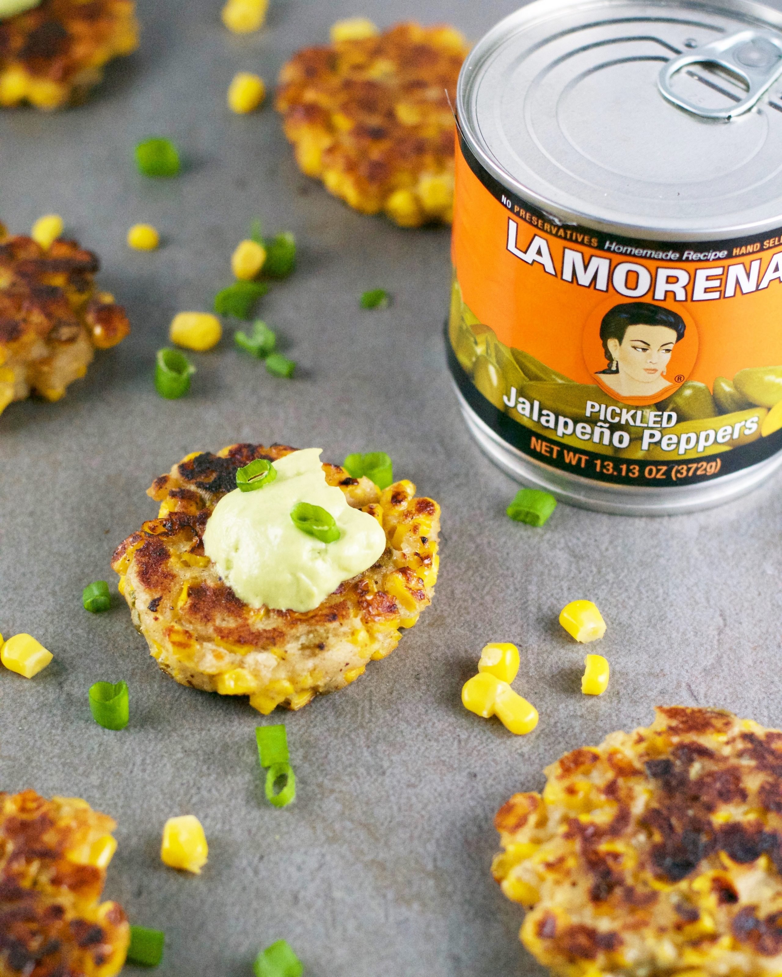 Corn jalapeño fritters with avocado crema and green onions with a can of pickled jalapeño peppers. 