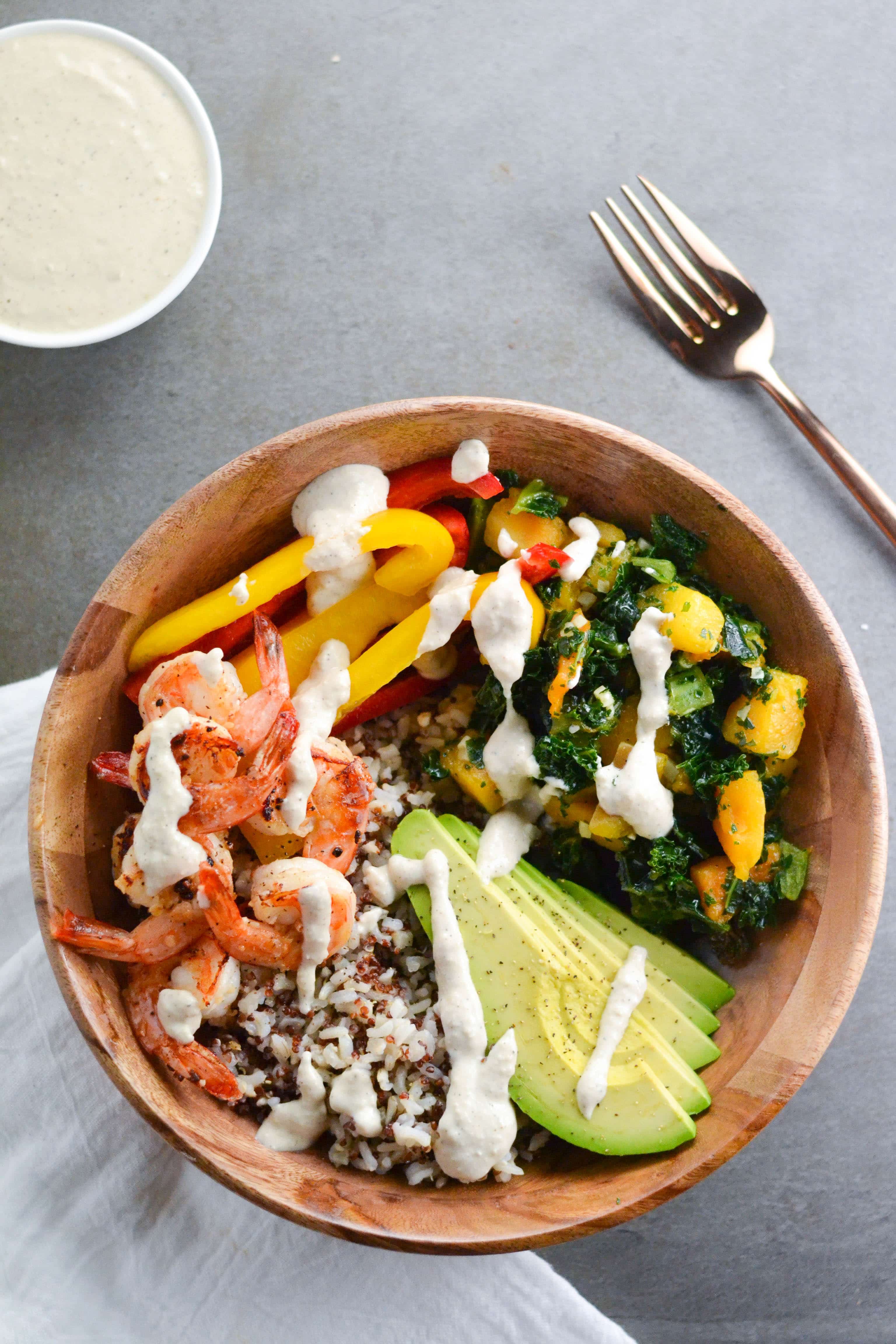 A bowl of a shrimp grain bowl with avocado, vegetables, rice and a creamy cashew sauce. 