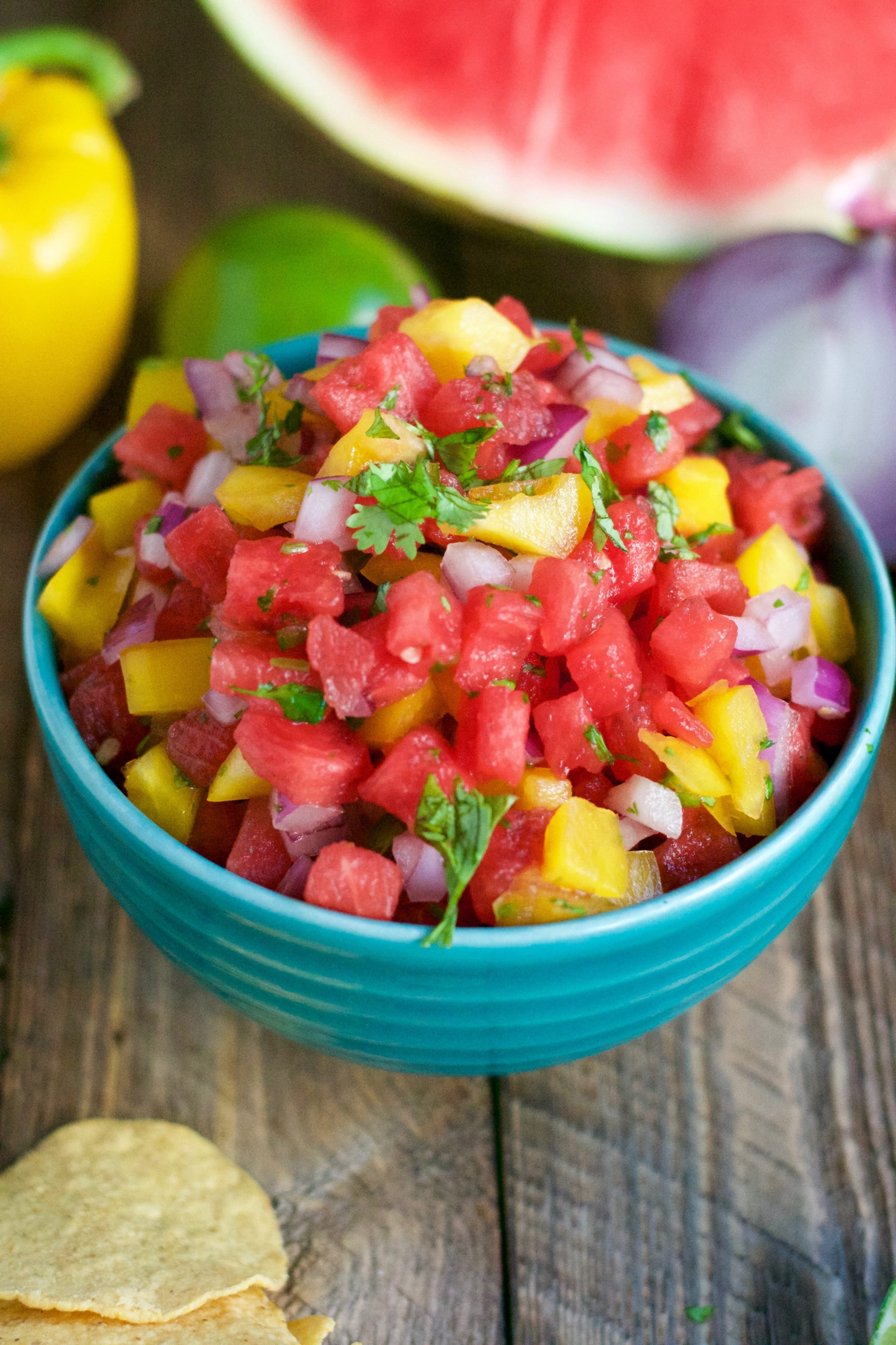 A bowl of watermelon salsa with yellow bell peppers and cilantro on a wooden table. 