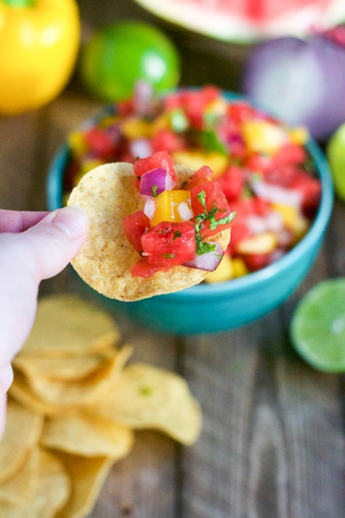 A hand holding a tortilla chip with watermelon salsa on it. 