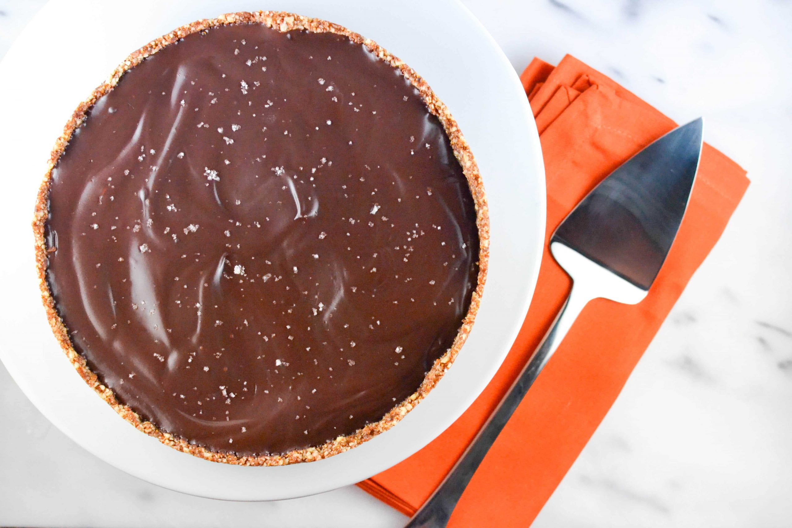 An overhead view of a chocolate pie with nut crust topped with fleur de sel and a pie server next to it. 