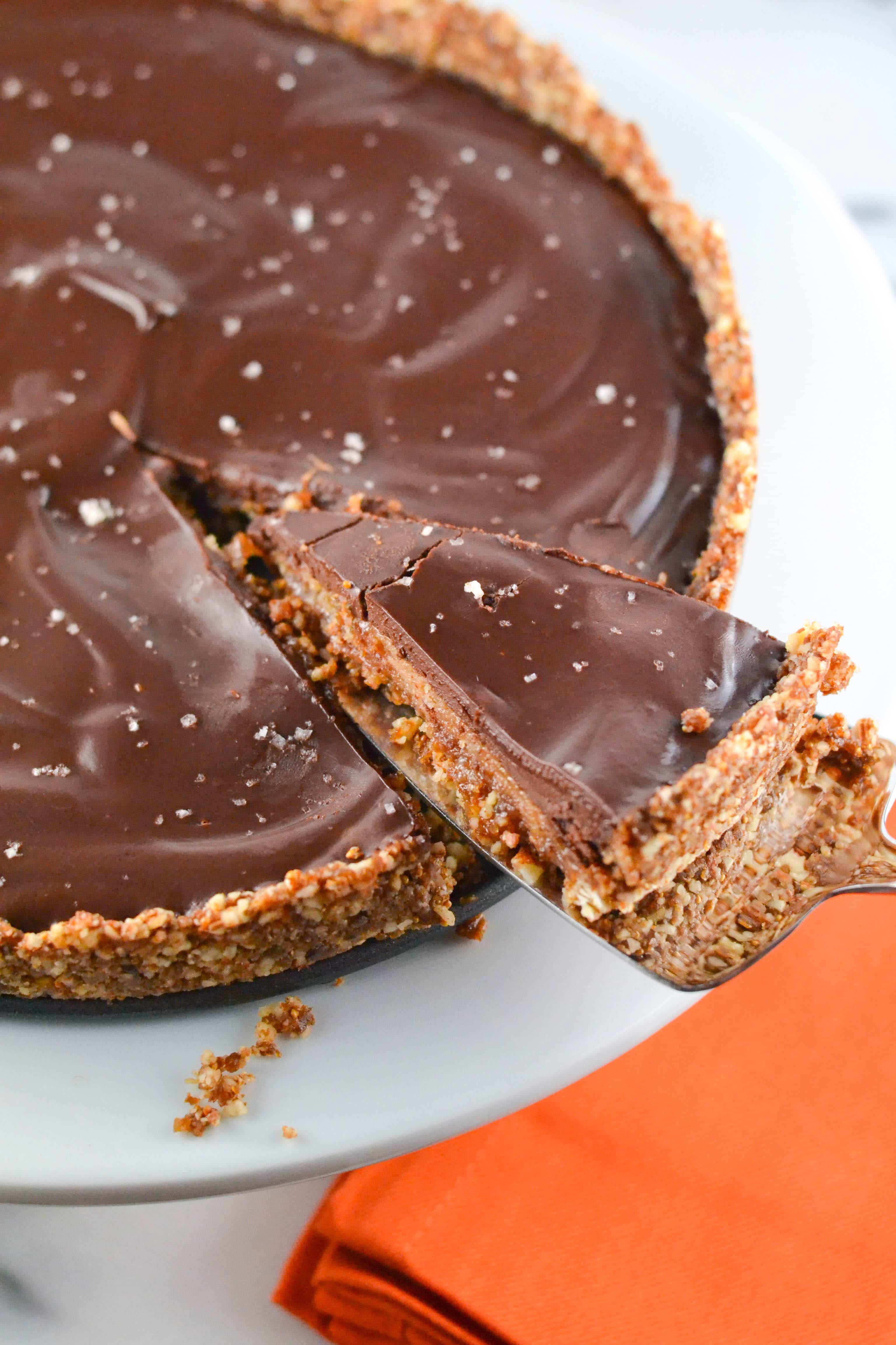A chocolate caramel pie with nut crust with a slice being taken out of it. 