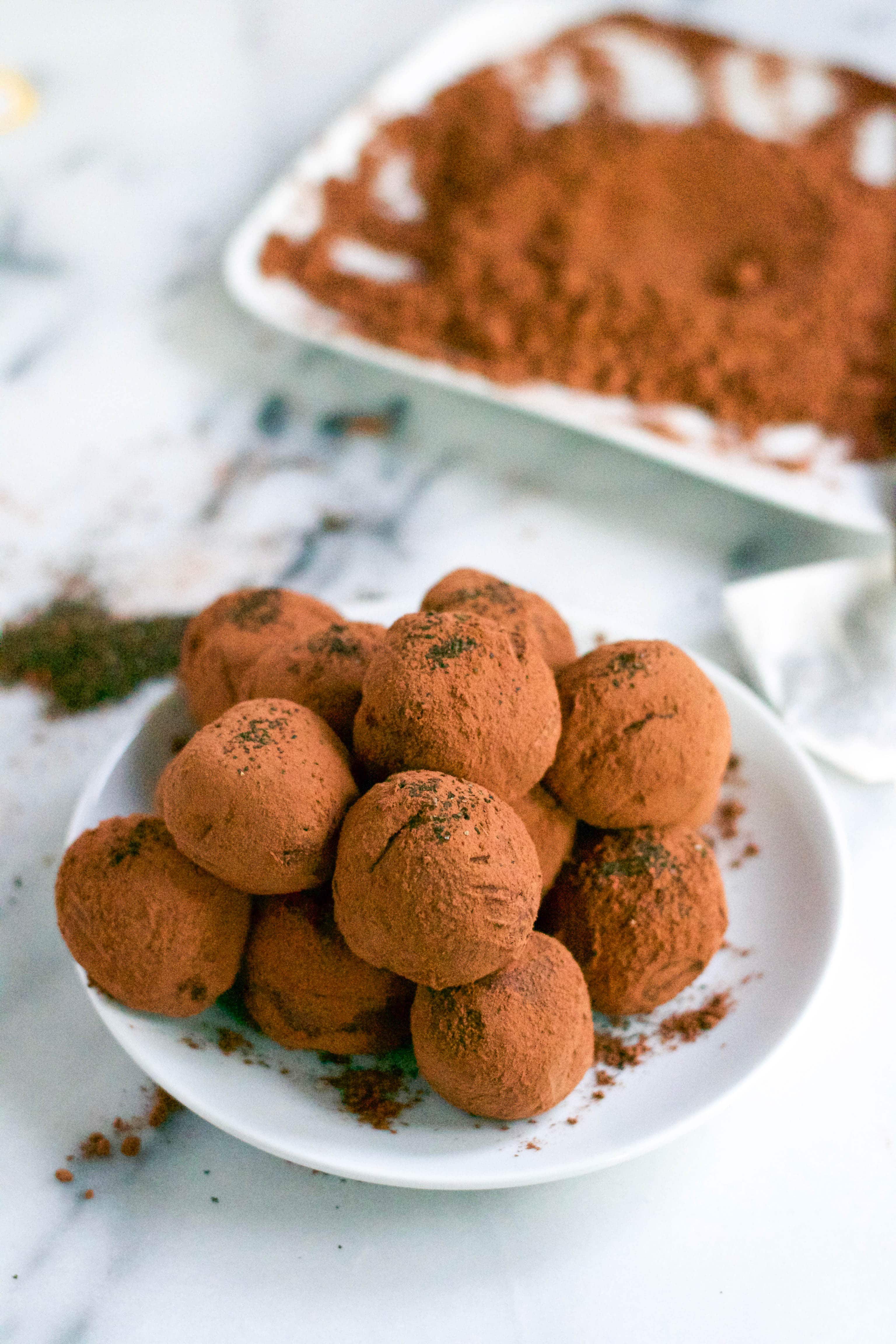 A plate of early grey chocolate truffles with a plate of cocoa powder in the background. 
