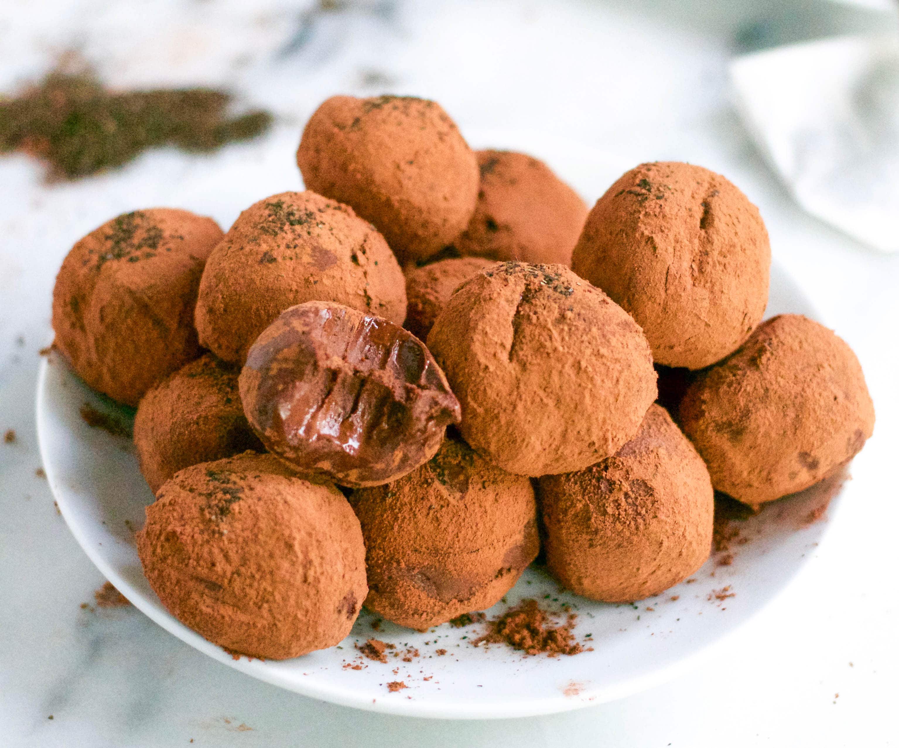 A pile of vegan earl grey chocolate truffles on a plate with a bite taken out of one of the truffles. 