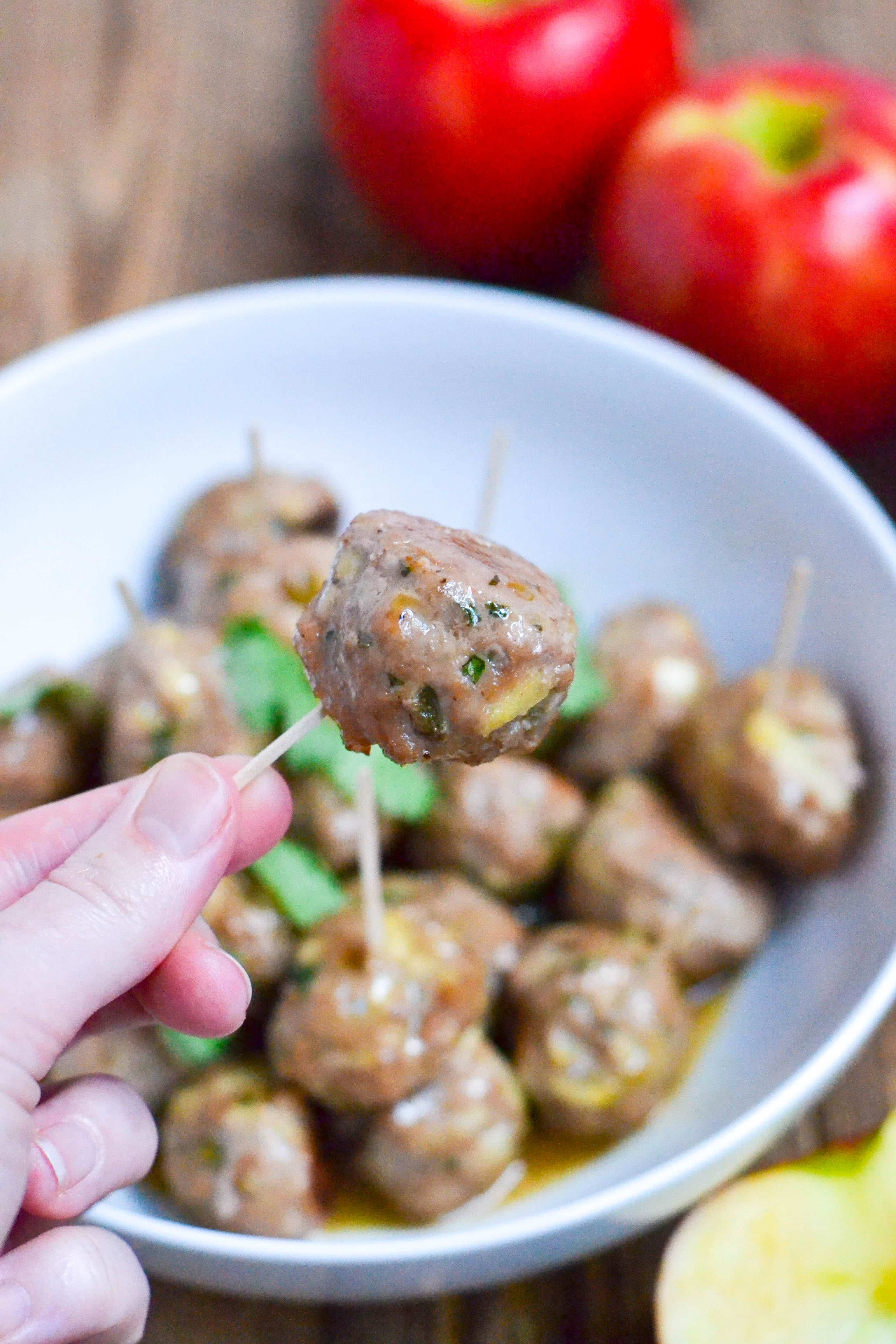 A hand holding a toothpick inserted into an apple jalapeño meatball. 