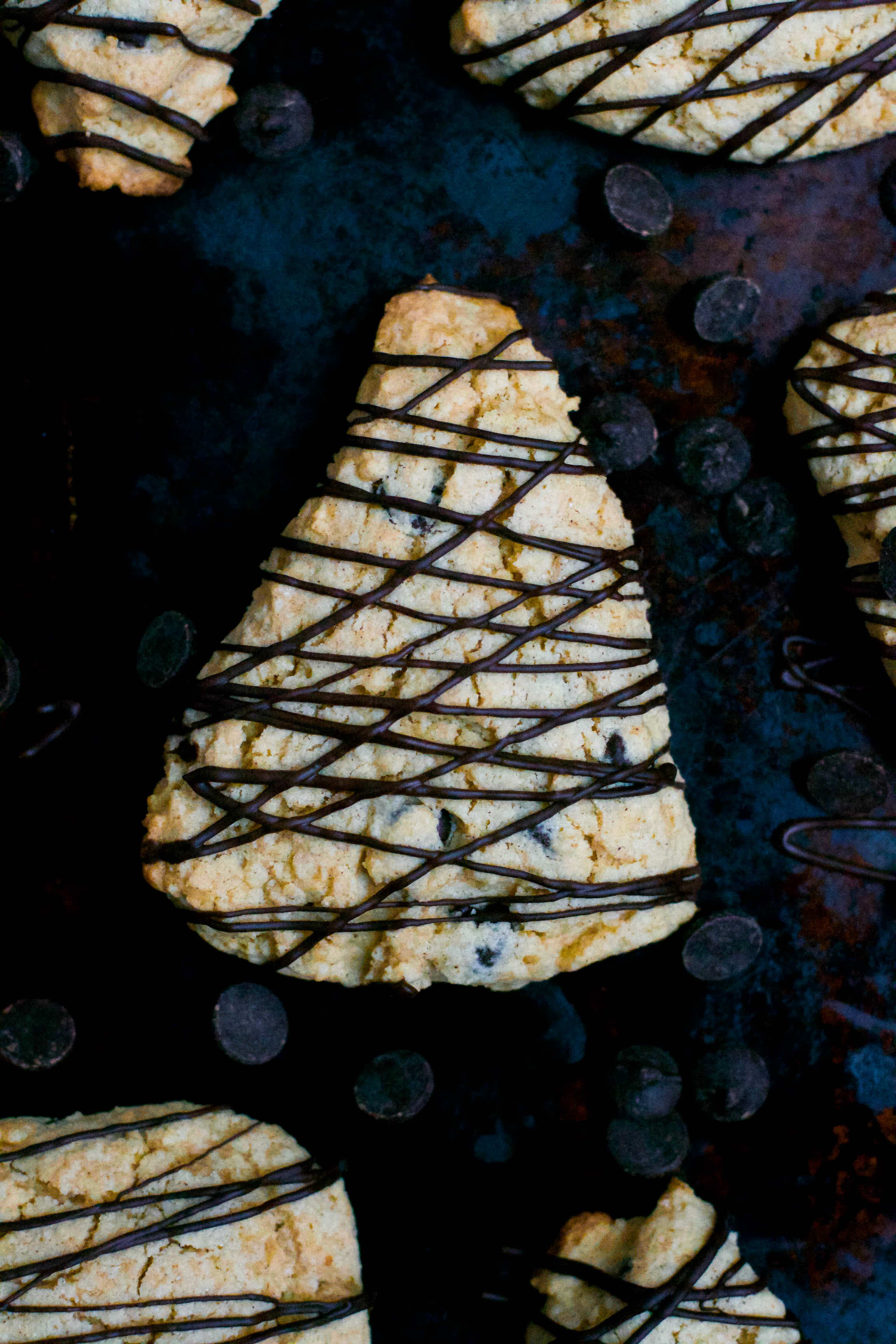 Overead view of chocolate chip scone triangles with a chocolate drizzle on a dark baking pan. 