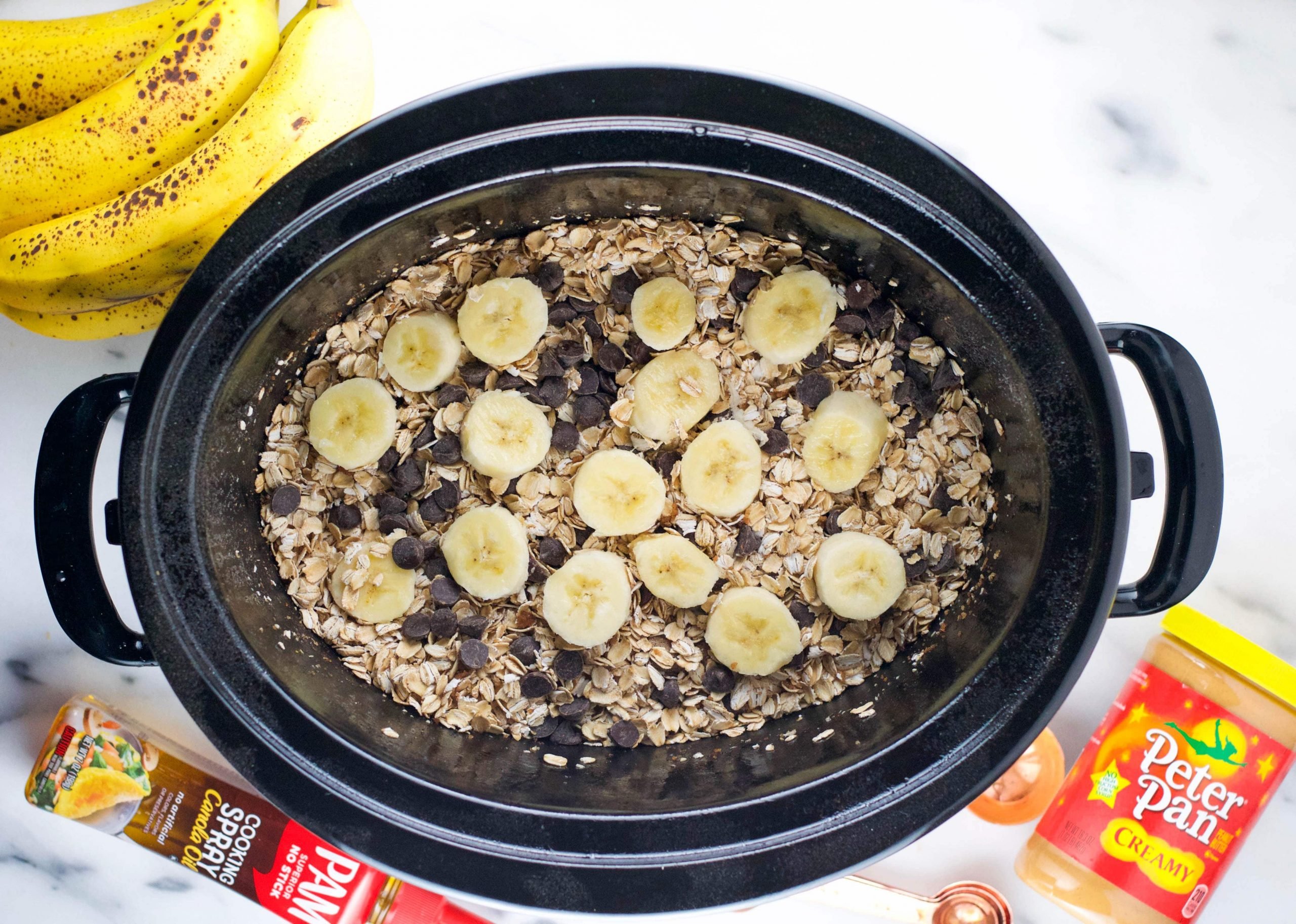 A slow cooker with oats, chocolate chips, and banana in it before cooking. 
