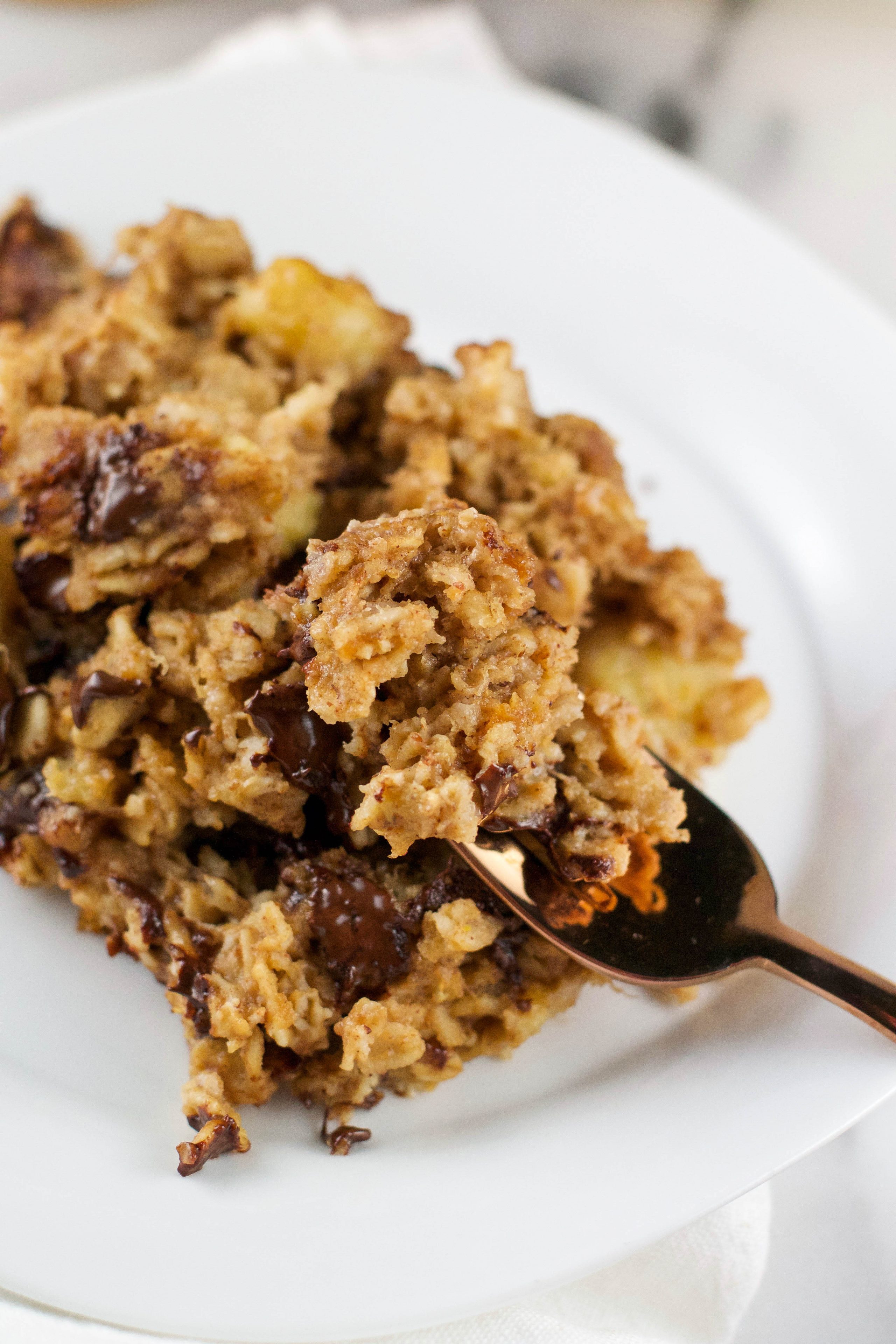 A plate of banana peanut butter baked oatmeal with chocolate chips on top and a spoon digging in. 