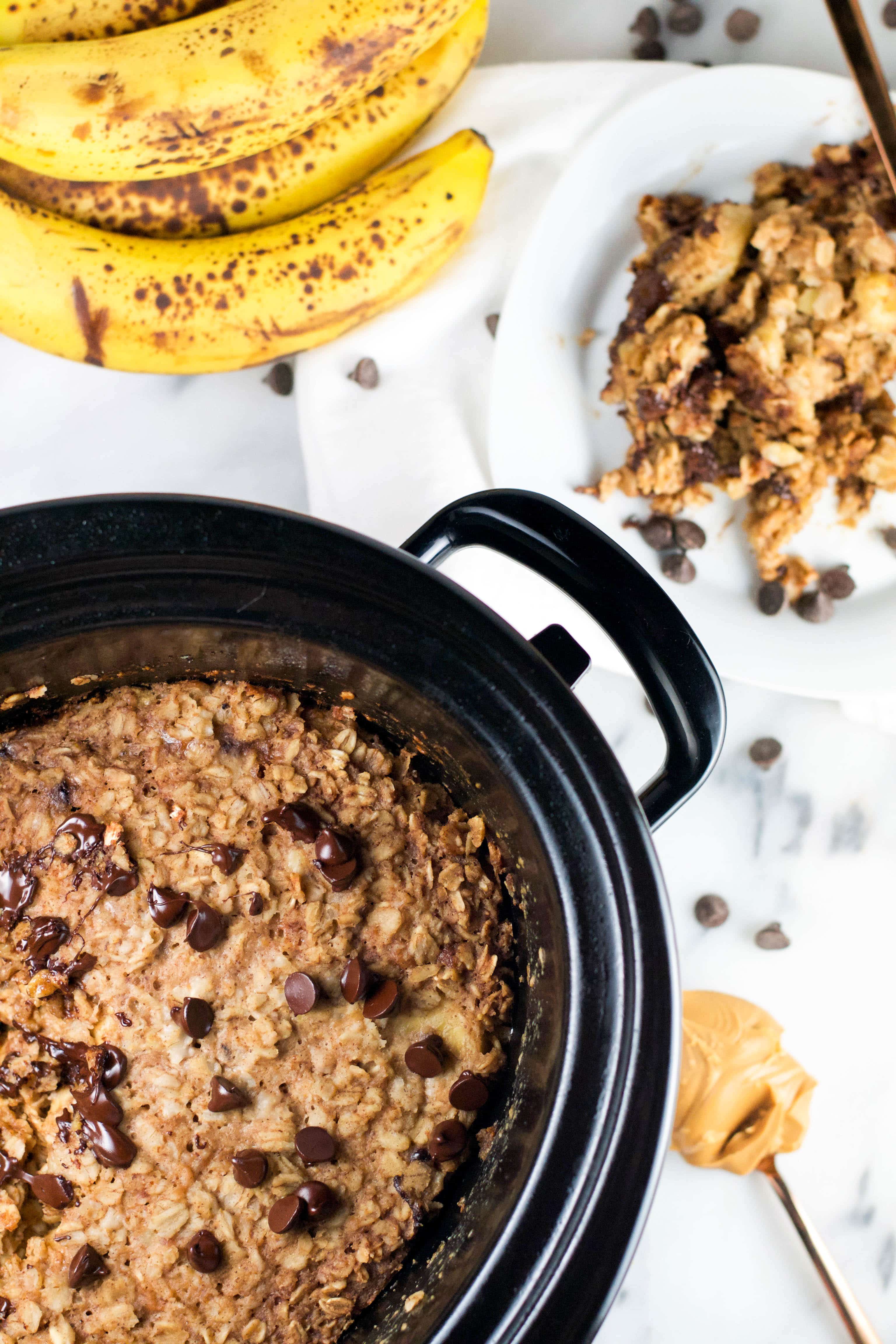 Baked oatmeal with chocolate chips in a slow cooker with bananas and peanut butter on the table. 