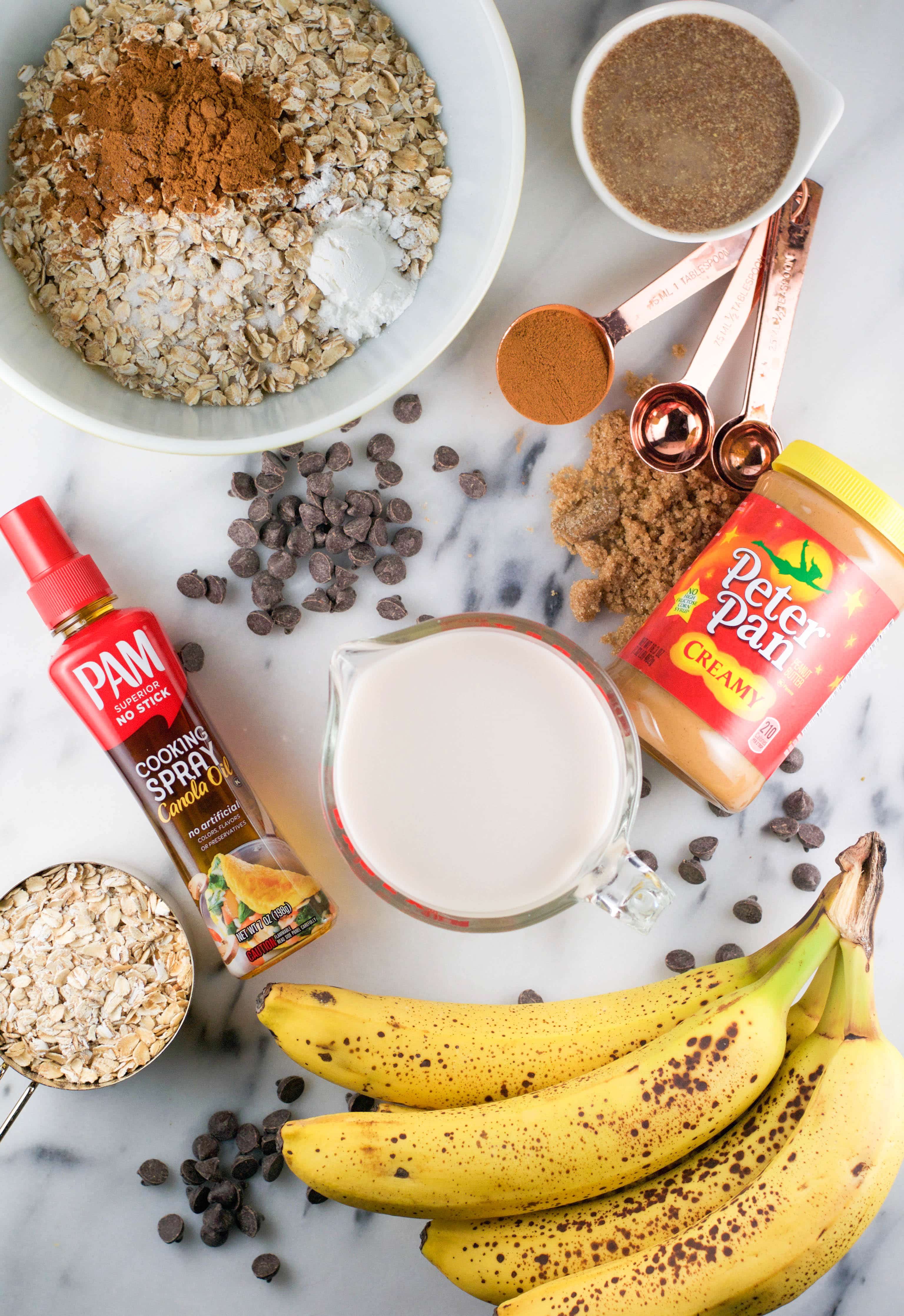 An overhead view of ingredients to make slow cooker banana peanut butter chocolate baked oatmeal including oats, flax seed, bananas, chocolate chips, cooking spray, and peanut butter. 