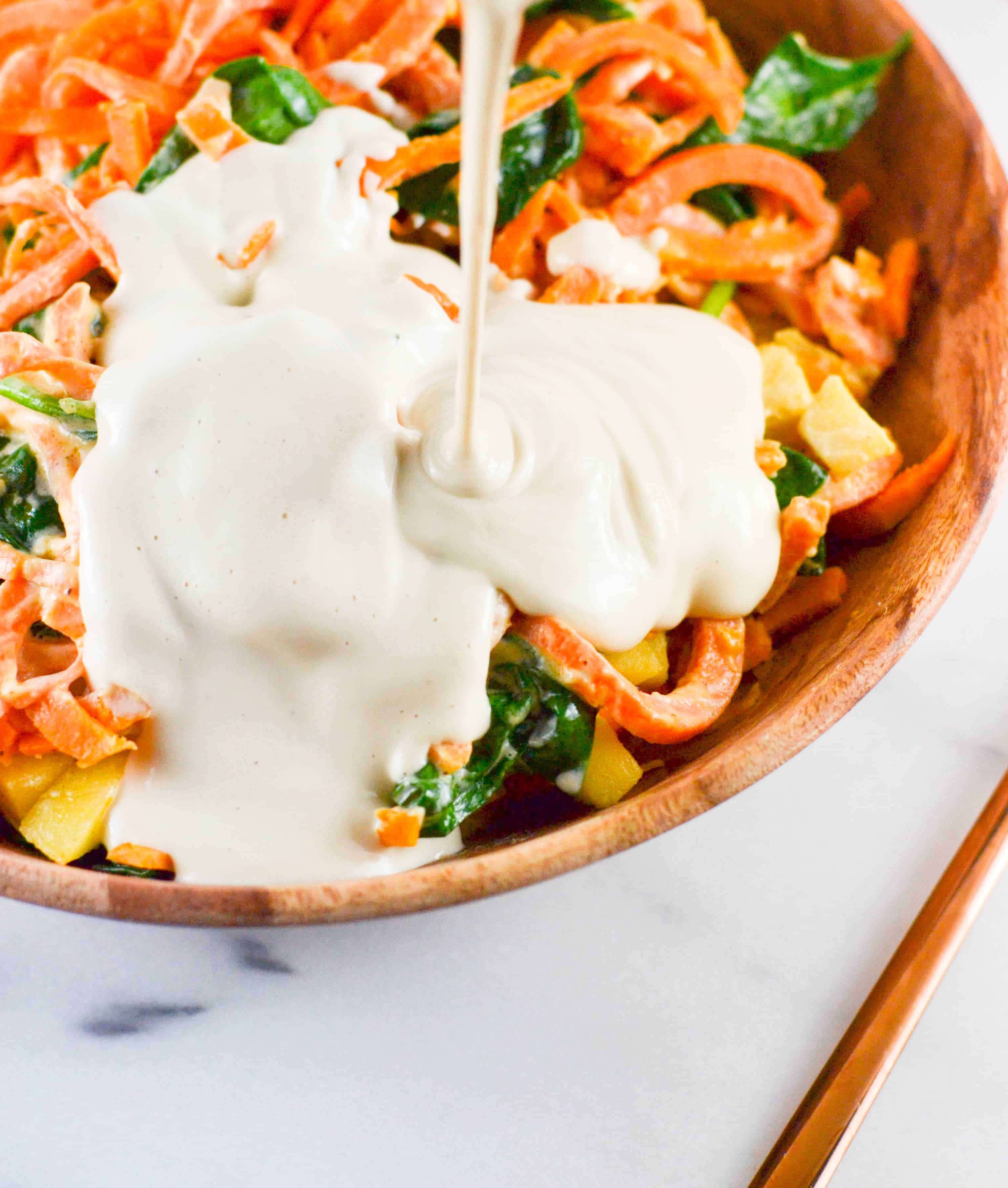 Creamy Cashew Sauce being drizzled over sweet potato noodles. 