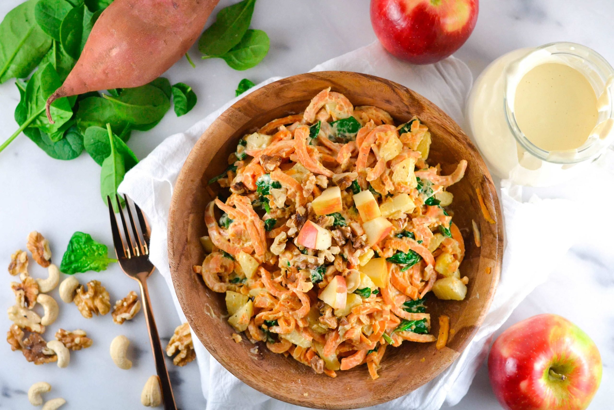 A wooden bowl of Sweet Potato Noodles in a Creamy Cashew Sauce topped with walnuts and apples. 