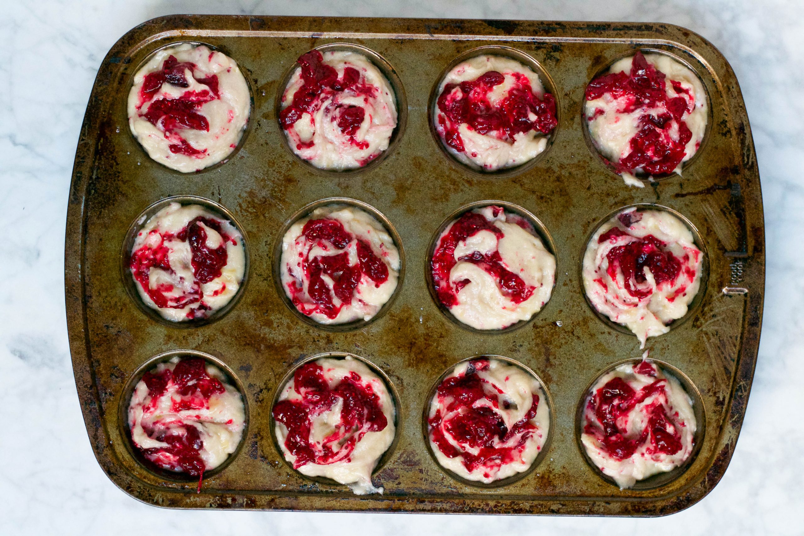 An overhead view of a muffin tin filled with banana cranberry muffin batter before baking. 