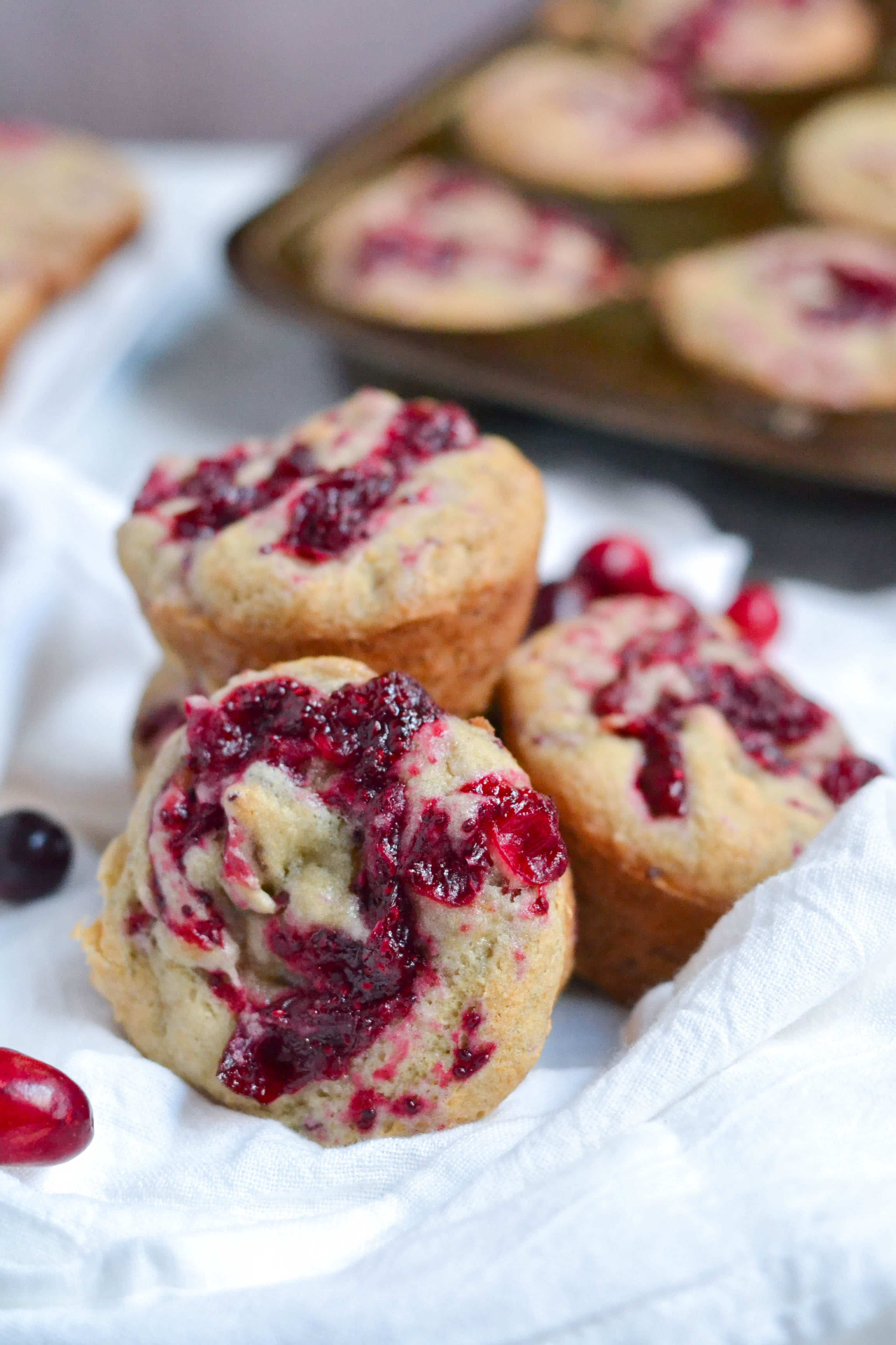 Three cranberry banana muffins layered on top of each other on a white linen. 