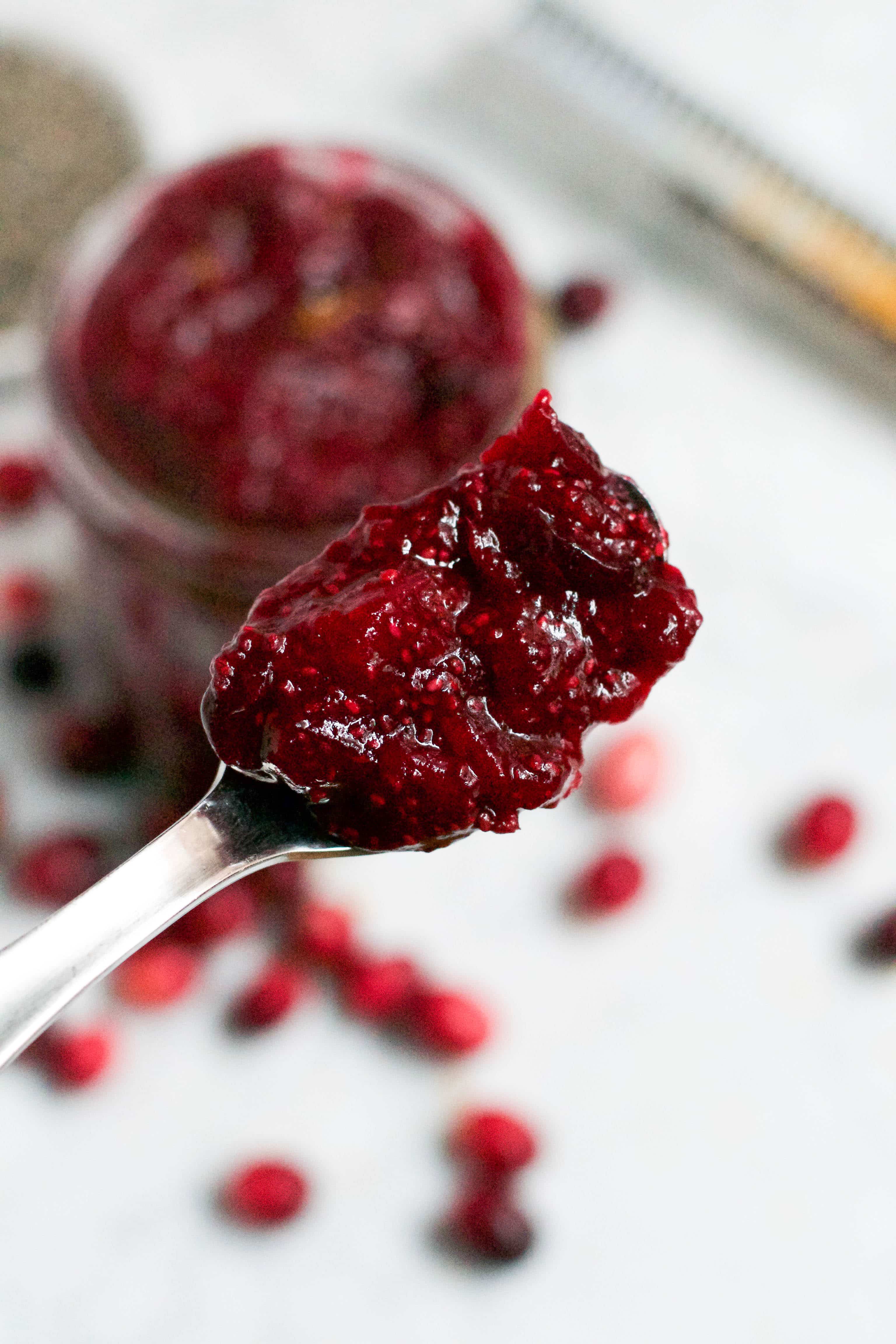 A spoon of cranberry orange chia jam with a jar in the background. 