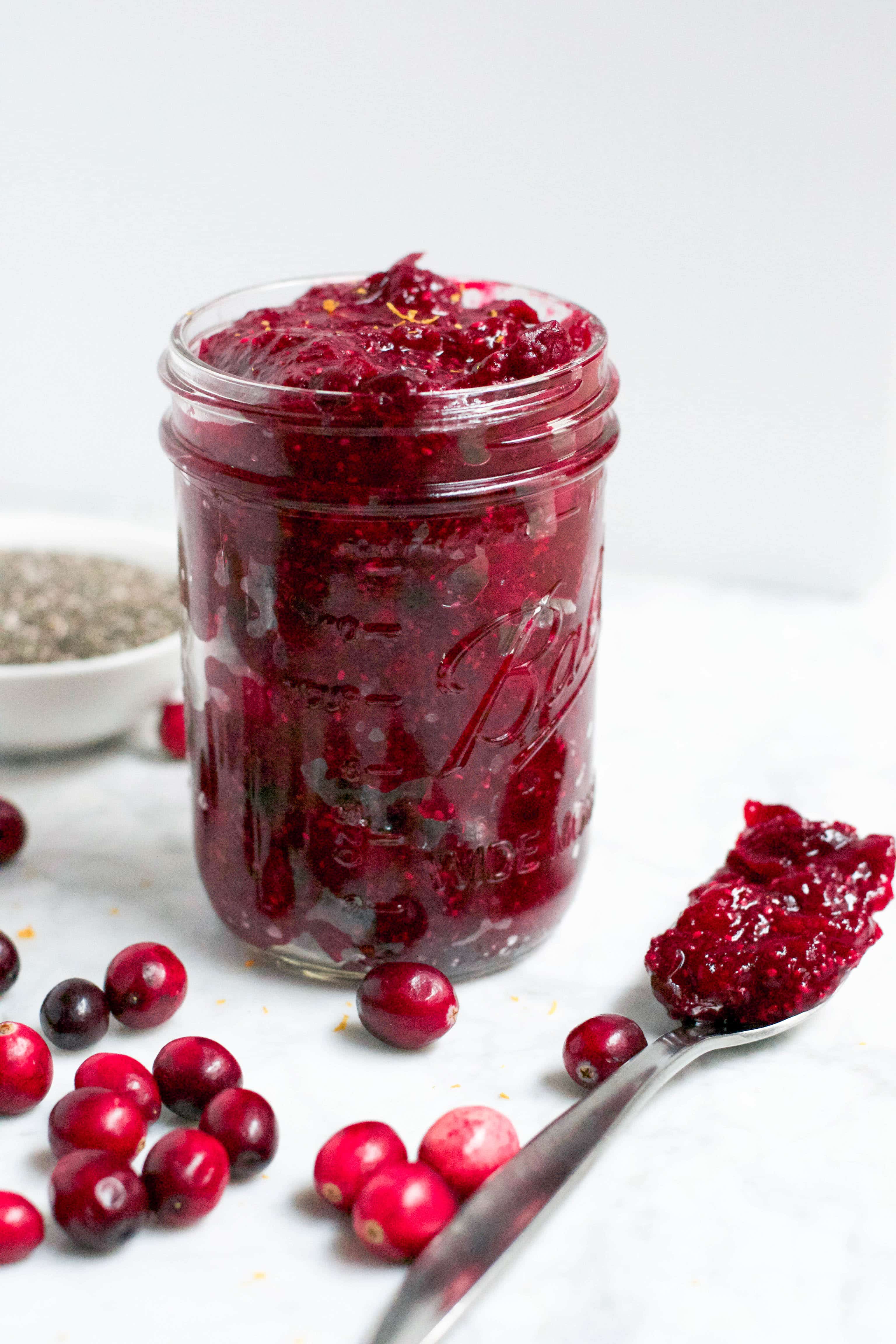 A jar of cranberry orange chia am with a spoon on the surface. 