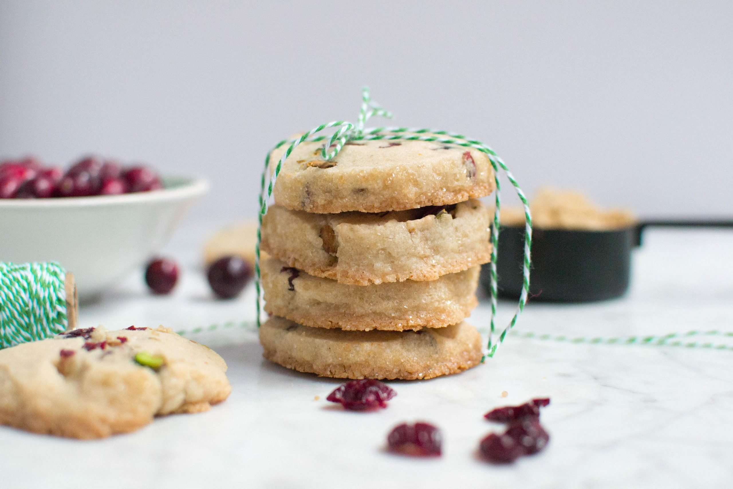 A stack of four pistachio cranberry shortbread cookies tied with green and white twine. 