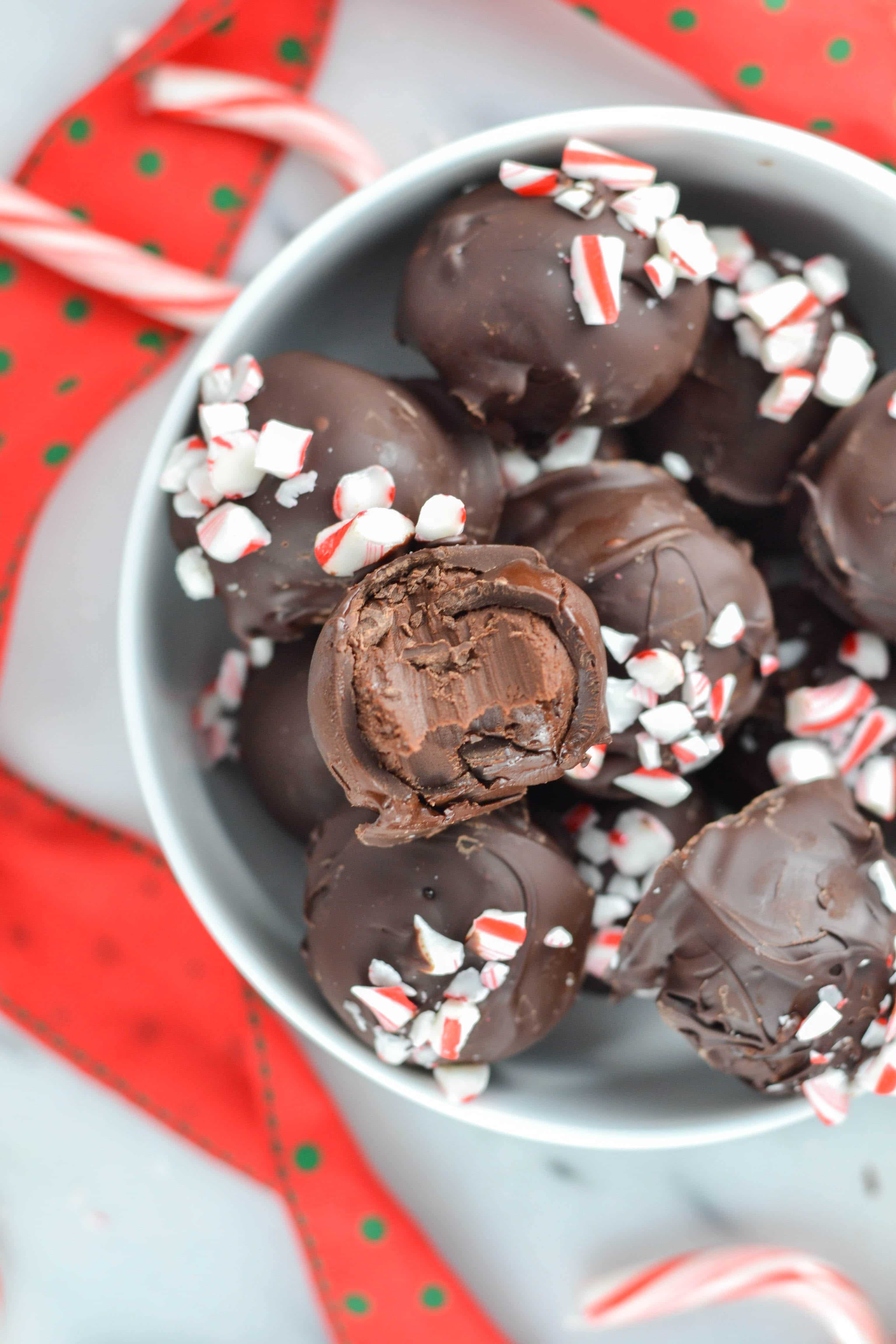 A bowl of vegan peppermint chocolate truffles with a bite taken out of one to show the creamy inside. 