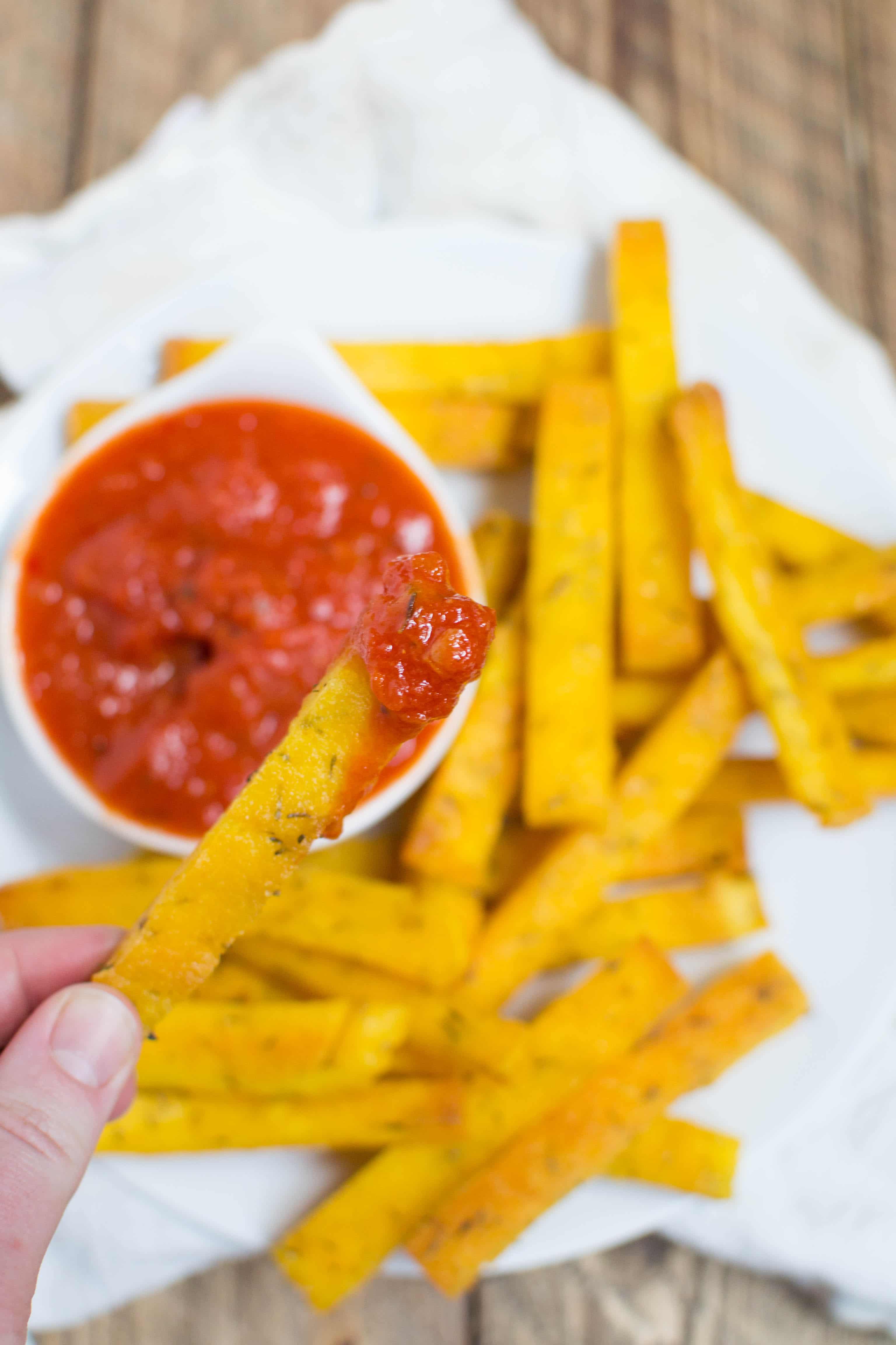 A hand holding a polenta fry that is dipped into marinara sauce.