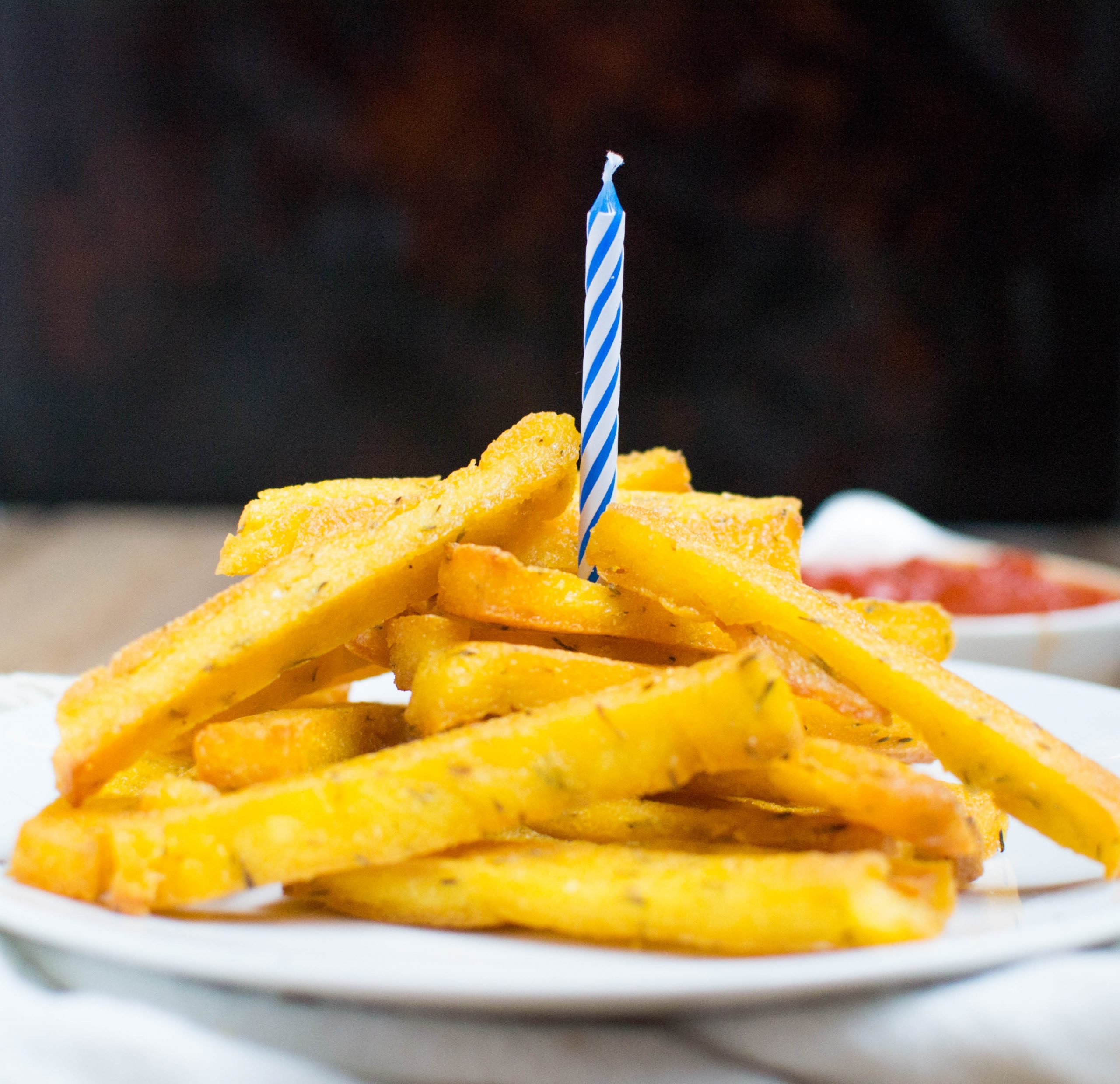 A mound of polenta fries with a birthday candle sticking out of it. 