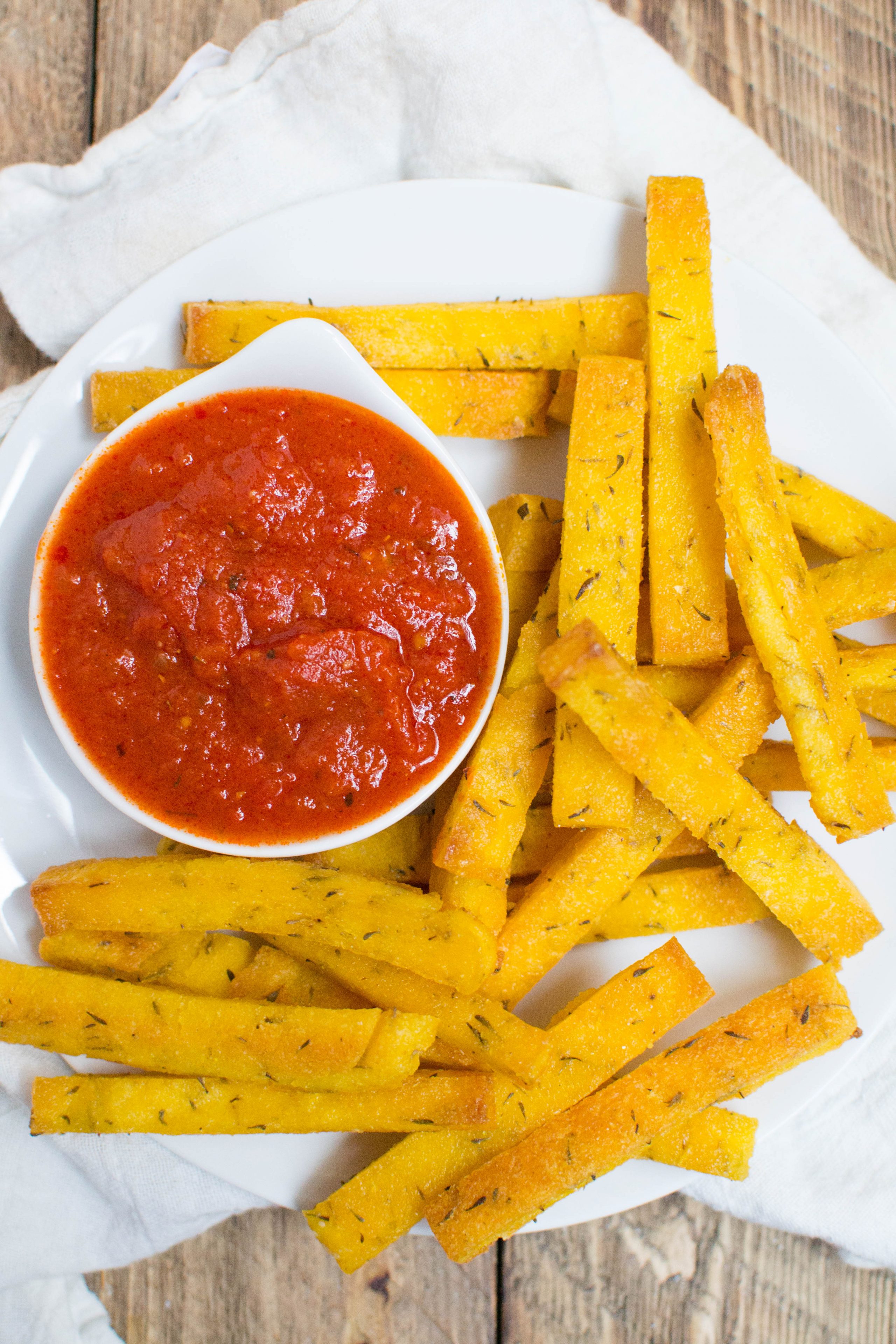 Polenta fries on a piece of parchment paper with a small bowl of marinara sauce. 