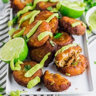 Fried mashed potato patties stuffed with taco seasoned ground beef and topped with avocado cream and fresh chopped cilantro on a white rectangular platter with fresh limes - fried potato and beef taco croquettes