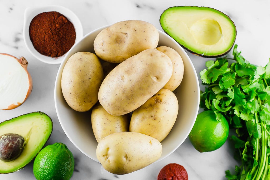 white potatoes in a bowl surrounded by avocado, lime, cilantro, taco seasonings, tomato paste