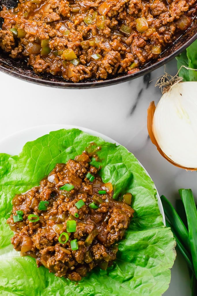 Sloppy Joe Lettuce Wraps (GF, DF) - ground beef flavored with tomato sauce, tamari sauce, mustard, apple cider vinegar, brown sugar cooked and sitting on top of a large green lettuce leaf topped with chopped green onion for serving and some ground beef in a skillet