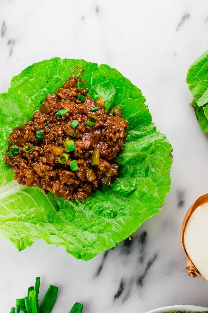 Sloppy Joe Lettuce Wraps - one gluten-free dairy-free sloppy joe lettuce wrap - a pile of ground beef flavored with tomato sauce, tamari, brown sugar, mustard, apple cider vinegar sitting on top of a large leaf of boston bibb lettuce and topped with fresh chopped green onions