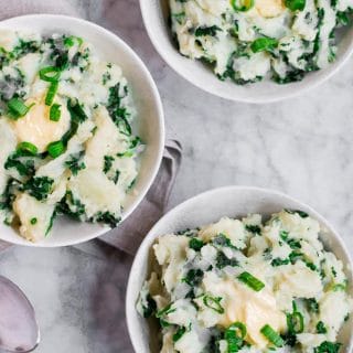 three bowls of dairy-free kale colcannon - mashed potatoes in a bowl mixed with green onion and dark green kale each topped with vegan butter on a marble table