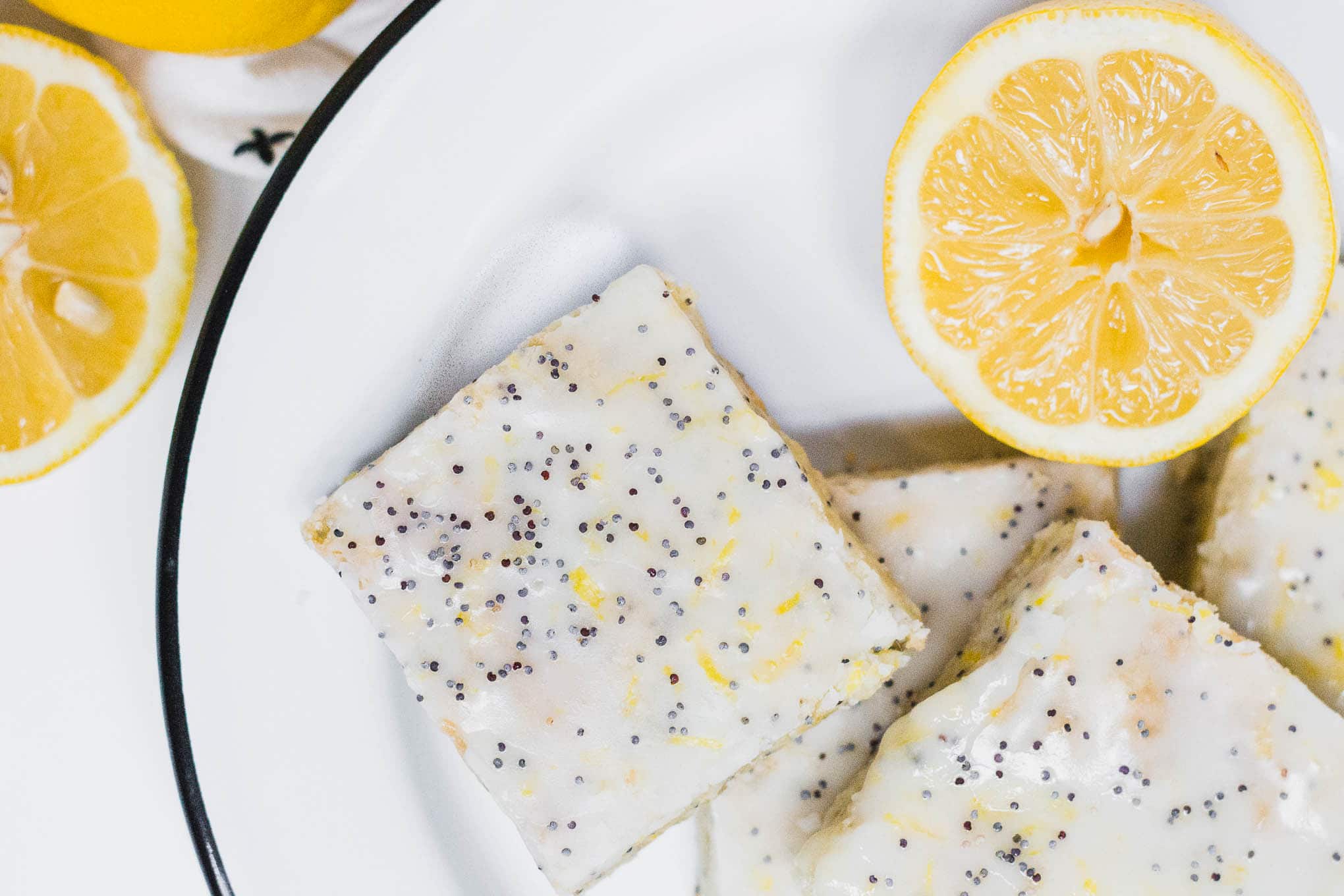 A white and back plate with a few gluten-free lemon poppy seed sugar cookie bars and half of a lemon in the upper right corner.