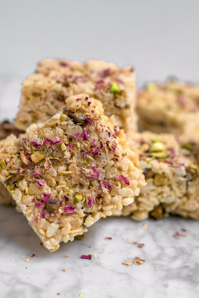 A stack of gluten-free rice cereal marshmallow treats with pistachios and rose petals on a marble table